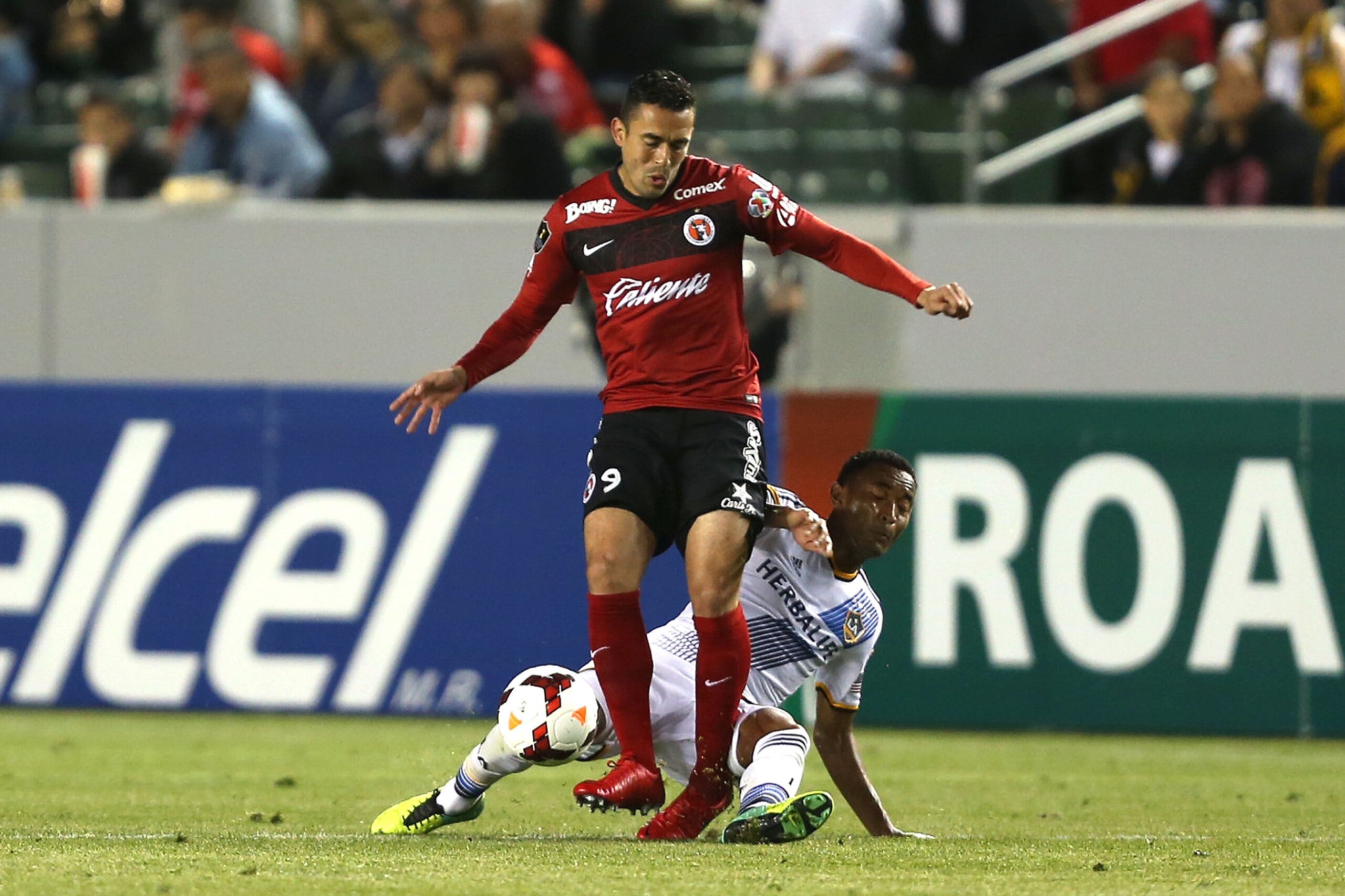 LOS ANGELES, CA - MARCH 12:  James Riley #26 of the Los Angeles Galaxy tackles Herculez Gomez #9 of Club Tijuana in the second half during the CONCACAF Champions League Quarterfinal match at StubHub Center on March 12, 2014 in Los Angeles, California.  (P