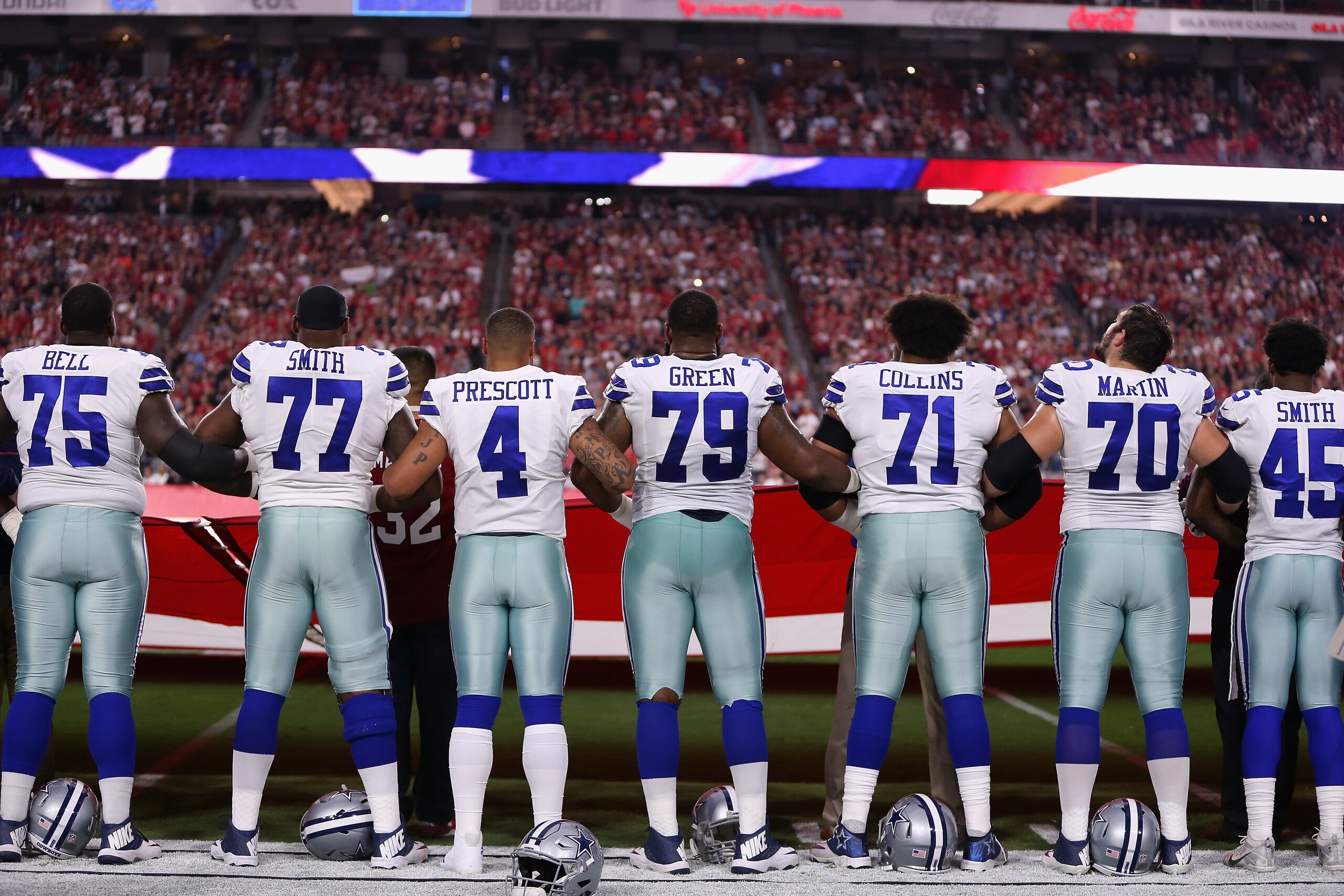 GLENDALE, AZ - SEPTEMBER 25: Quarterback Dak Prescott #4 of the Dallas Cowboys links arms with teammates offensive tackle Tyron Smith #77 and offensive guard Chaz Green #79 during the National Anthem before the start of the NFL game against the Arizona Ca
