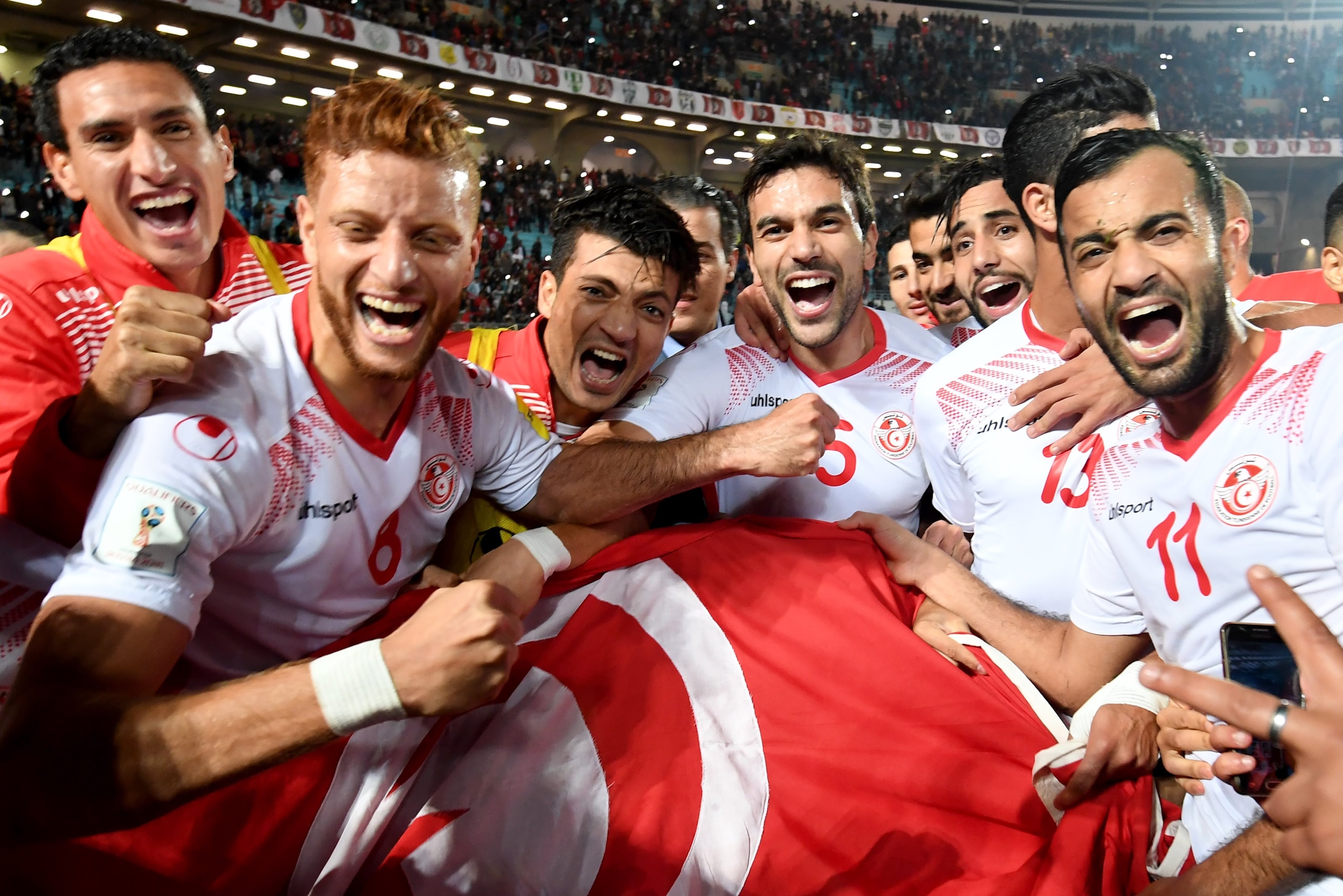 Players of the Tunisian national football team celebrate with their national flag after qualifying for the 2018 World Cup finals after drawing their qualifiers match against Libya at the Rades Olympic Stadium in the capital Tunis on November 11, 2017. / A