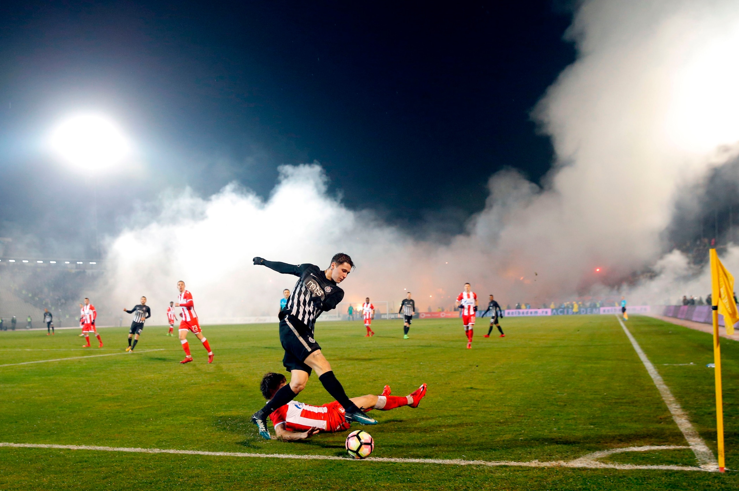 TOPSHOT - Partizan's Marko Jevtovic (L) vies with Crvena Zvezda's Filip Stojkovic (bottom) as smoke rise from the stands during the Serbian Superleague derby football match between Partizan Belgrade and Crvena Zvezda (Red Star), on December 13, 2017 in Be