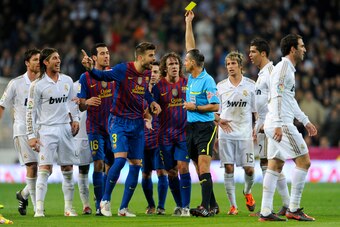 Referee Cesar Muniz Fernandez shows the yellow card to Barcelona's defender Gerard Pique (C) during the Spanish Cup 'El clasico' football match Real Madrid vs Barcelona at the Santiago Bernabeu stadium in Madrid on January 18, 2012. AFP PHOTO/ DANI POZO (