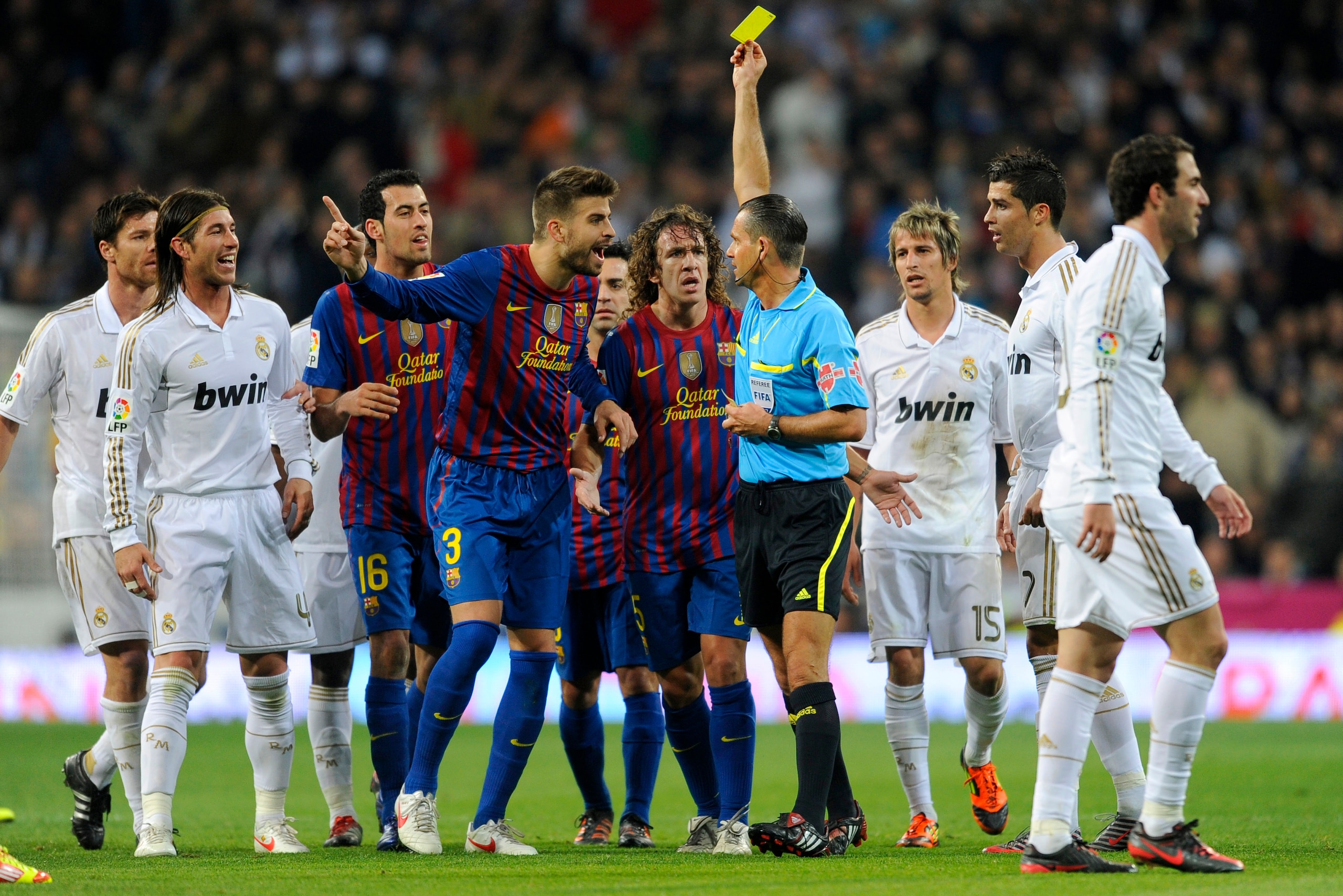 Referee Cesar Muniz Fernandez shows the yellow card to Barcelona's defender Gerard Pique (C) during the Spanish Cup 'El clasico' football match Real Madrid vs Barcelona at the Santiago Bernabeu stadium in Madrid on January 18, 2012. AFP PHOTO/ DANI POZO (
