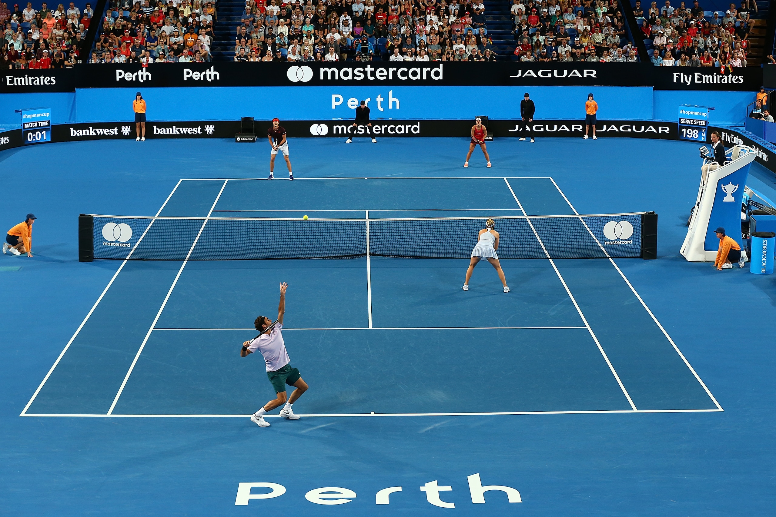 PERTH, AUSTRALIA - JANUARY 06: Roger Federer of Switzerland, partnered with Belinda Bencic of Switzerland serves to Angelique Kerber of Germany, partnered with Alexander Zverev during the mixed doubles finals match against on day eight during the 2018 Hop