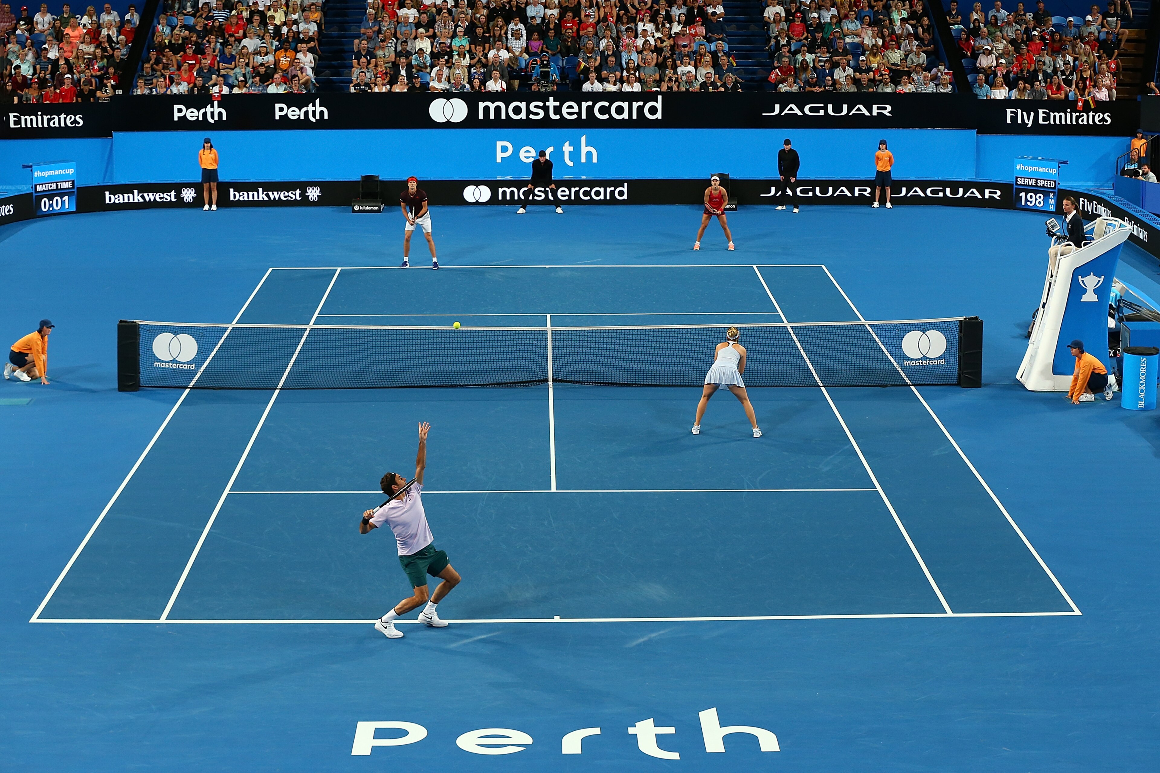 PERTH, AUSTRALIA - JANUARY 06: Roger Federer of Switzerland, partnered with Belinda Bencic of Switzerland serves to Angelique Kerber of Germany, partnered with Alexander Zverev during the mixed doubles finals match against on day eight during the 2018 Hop