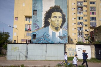 A familly passes by a wall painted with a portrait of Italian Juventus FC player Argentinian Carlos Tevez in Barrio Ejercito de los Andes, better known as Fuerte Apache, in the outskirts of Buenos Aires, Argentina, on June 04, 2015, ahead of Saturday's Ba