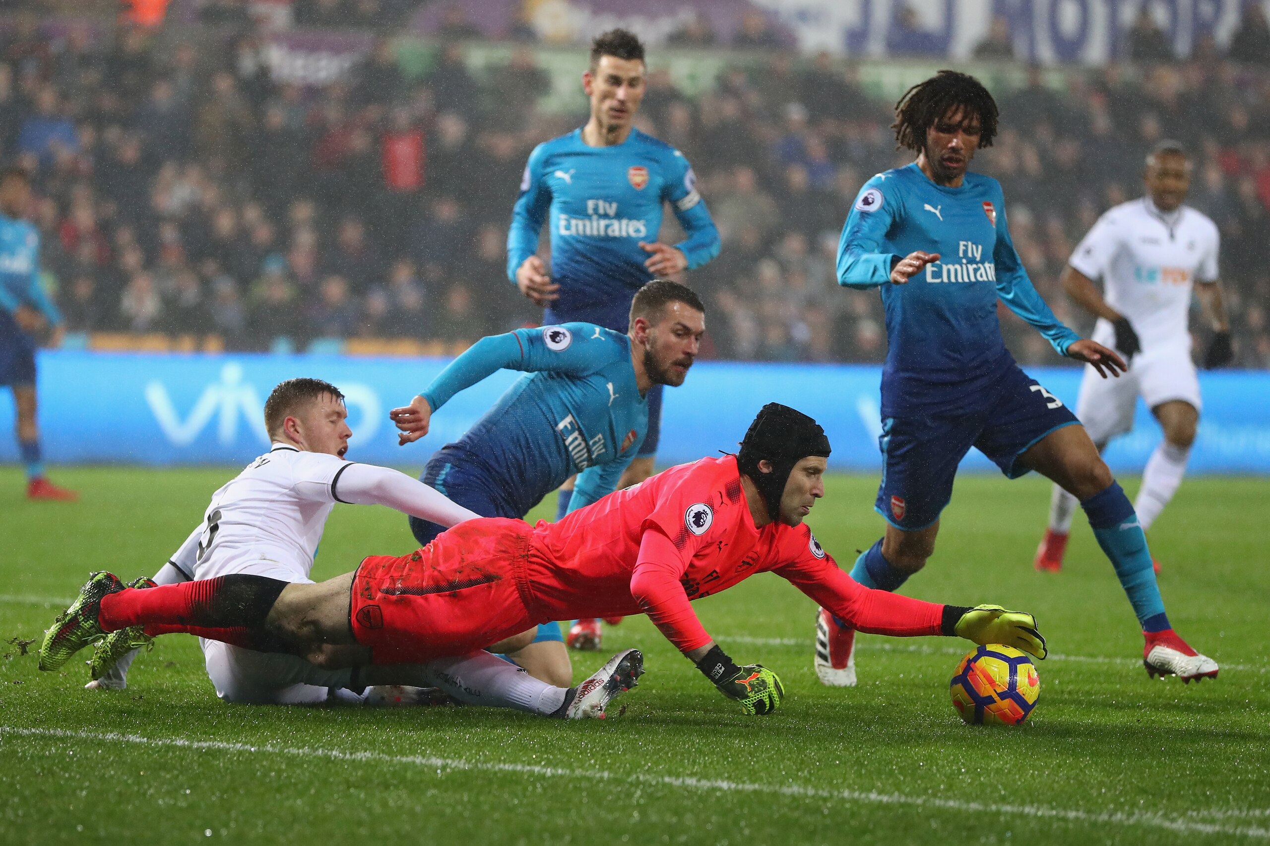 SWANSEA, WALES - JANUARY 30: Petr Cech the goalkeeper of Arsenal dives on the ball as Shkodran Mustafi and Mohamed Elneny and Alfie Mawson of Swansea City look on during the Premier League match between Swansea City and Arsenal at Liberty Stadium on Janua