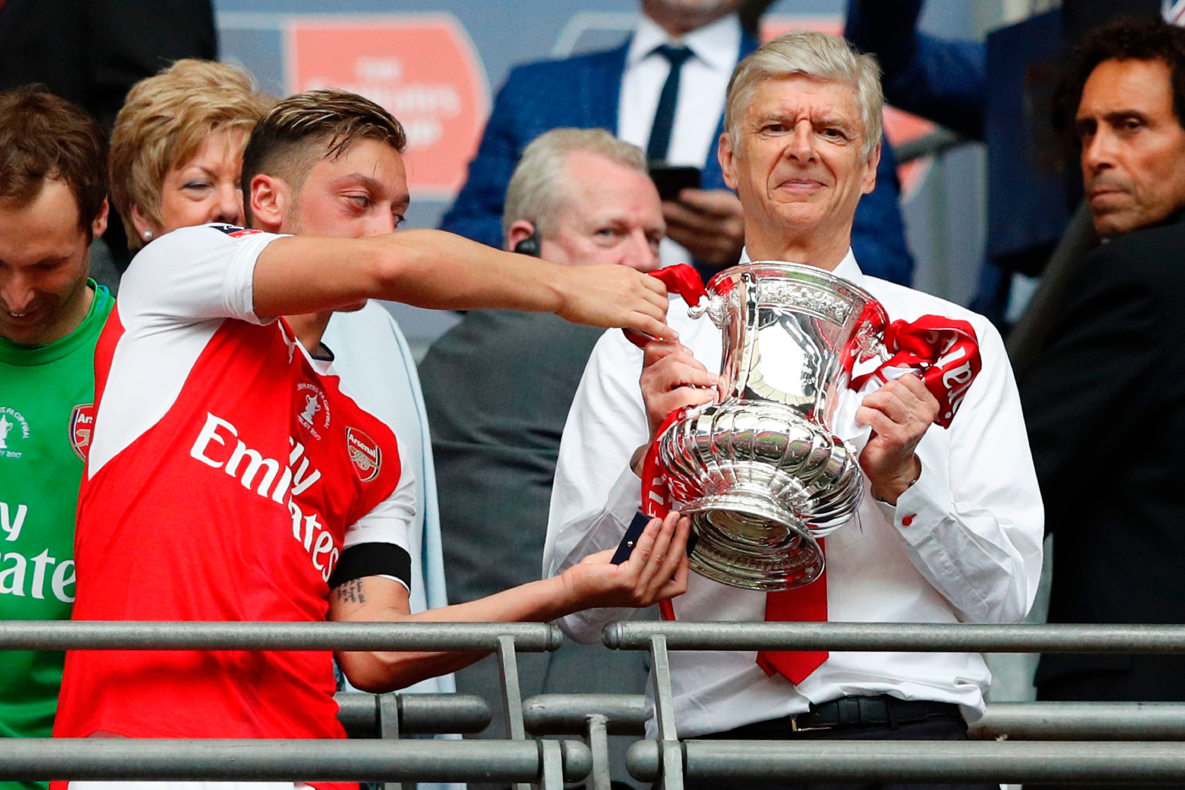 Arsenal's German midfielder Mesut Ozil (L) hands over the FA Cup trophy to Arsenal's French manager Arsene Wenger after their win over Chelsea in the English FA Cup final football match between Arsenal and Chelsea at Wembley stadium in London on May 27, 2
