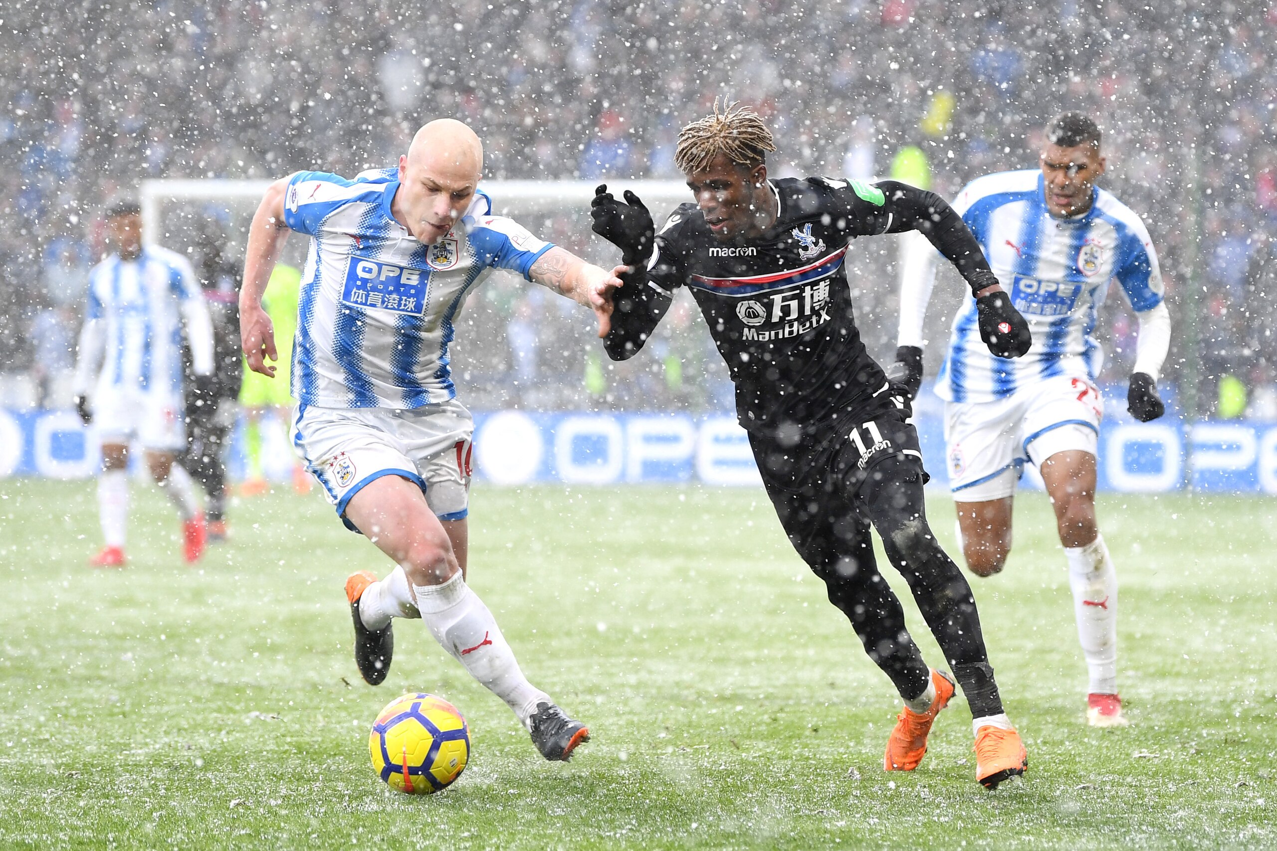 HUDDERSFIELD, ENGLAND - MARCH 17: Wilfried Zaha of Crystal Palace is challenged by Aaron Mooy of Huddersfield Town during the Premier League match between Huddersfield Town and Crystal Palace at John Smith's Stadium on March 17, 2018 in Huddersfield, Engl