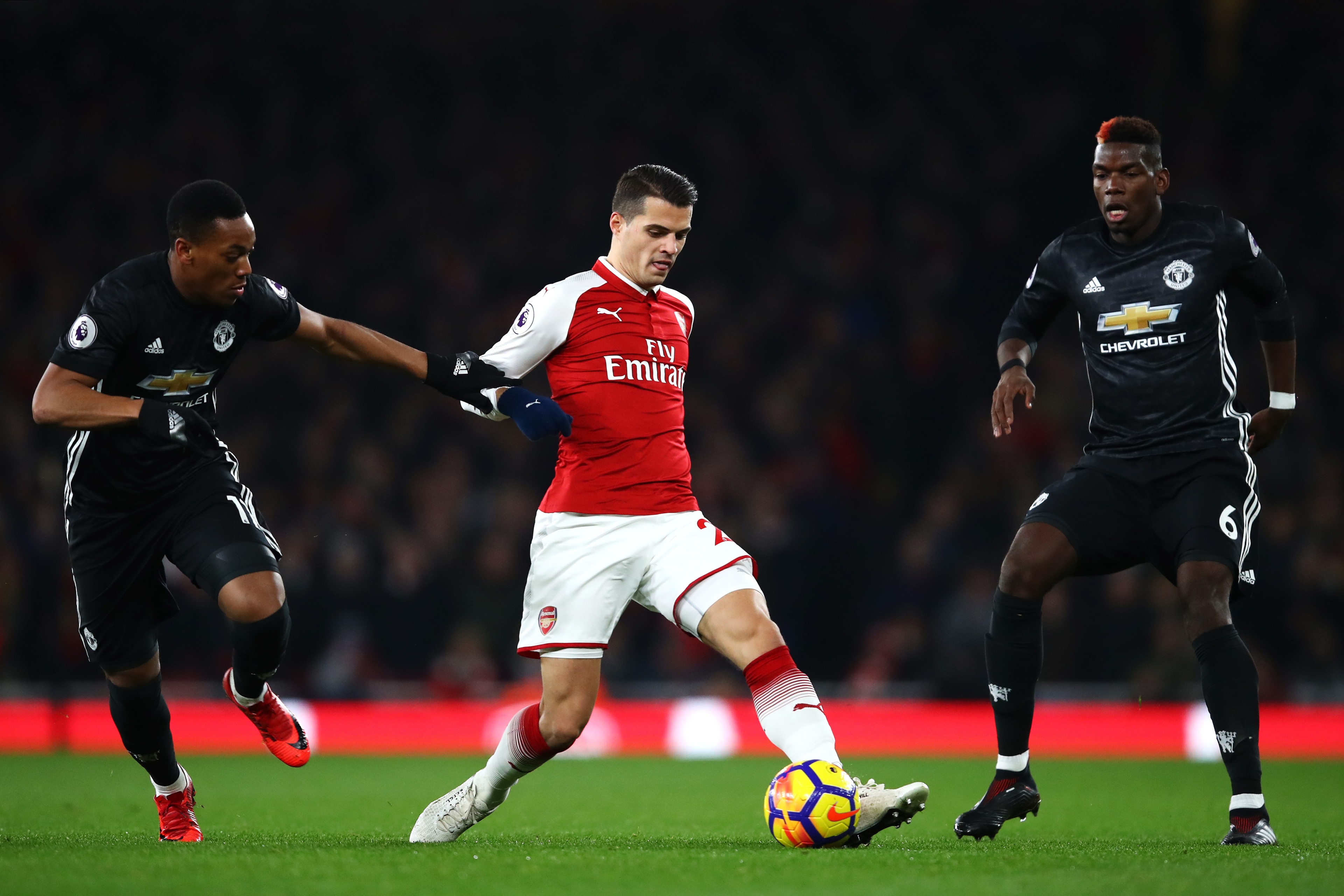 LONDON, ENGLAND - DECEMBER 02:  Granit Xhaka of Arsenal is challenged by Anthony Martial of Manchester United (L) and Paul Pogba of Manchester United (R) during the Premier League match between Arsenal and Manchester United at Emirates Stadium on December