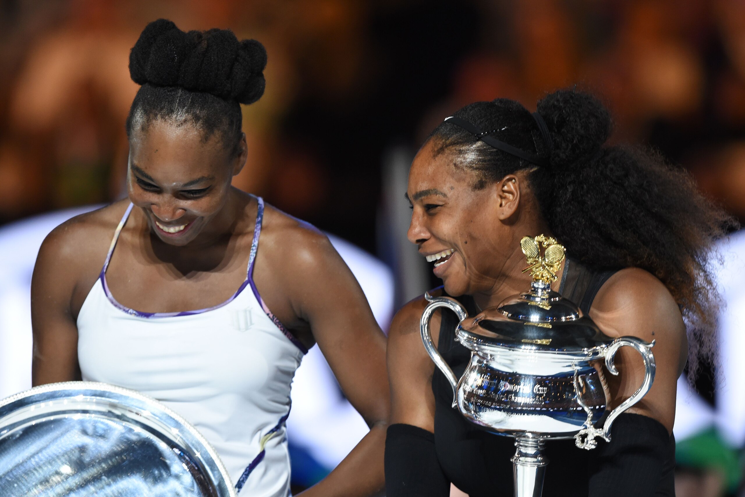 Serena Williams of the US (R) holds the winner's trophy as she laughs with her sister Venus Williams of the US (L) at the awards ceremony for the women's singles final on day 13 of the Australian Open tennis tournament in Melbourne on January 28, 2017.  /