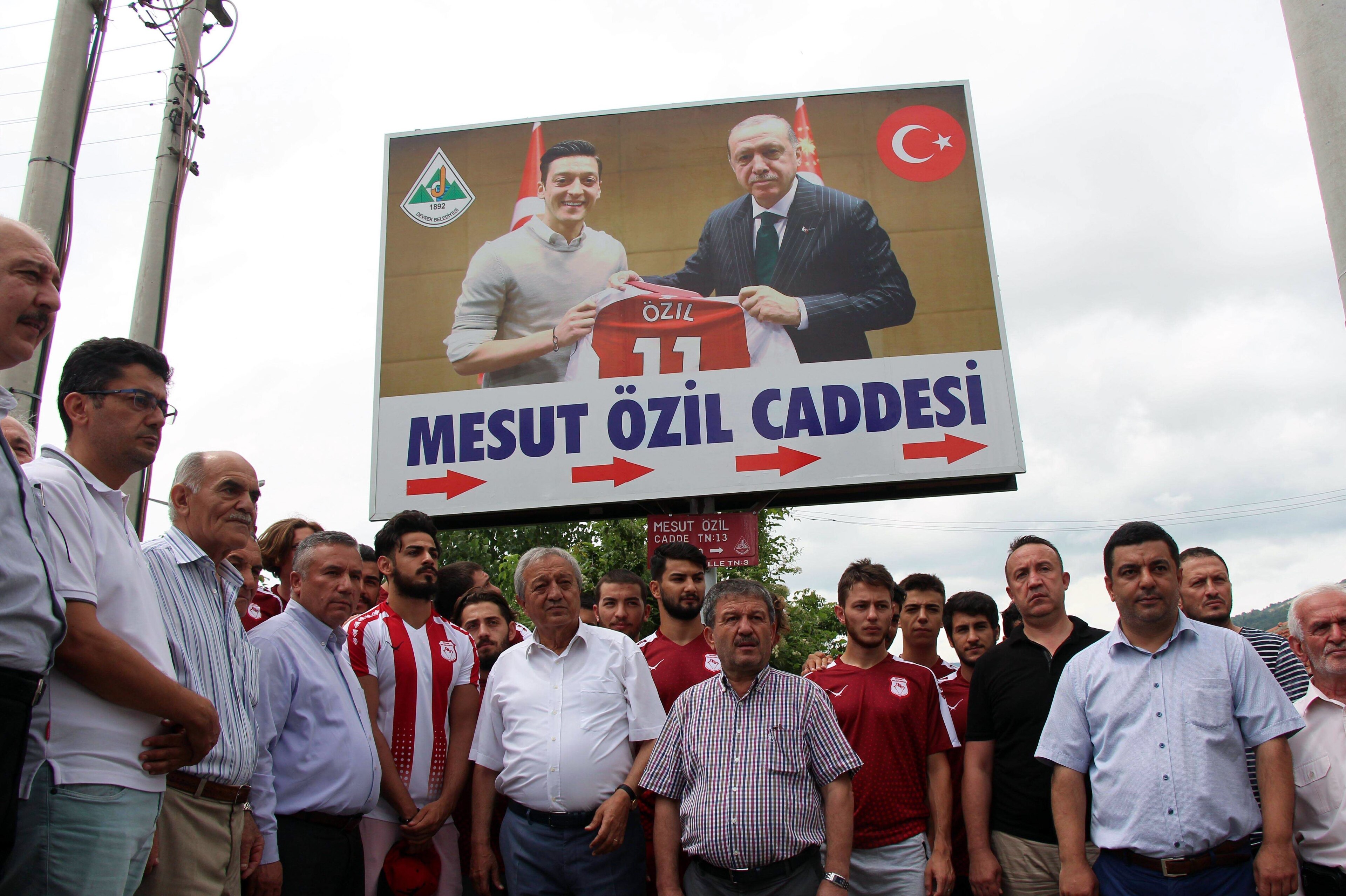 People gather under a cardboard bearing a photo of German national team football player Mesut Ozil (L) and Turkish President Recep Tayyip Erdogan (R) reading ' Mesut Ozil street' on July 24, 2018 during a street name ceremony in Zonguldak's Devrek distric People gather under a cardboard bearing a photo of German national team football player Mesut Ozil (L) and Turkish President Recep Tayyip Erdogan (R) reading ' Mesut Ozil street' on July 24, 2018 during a street name ceremony in Zonguldak's Devrek distric