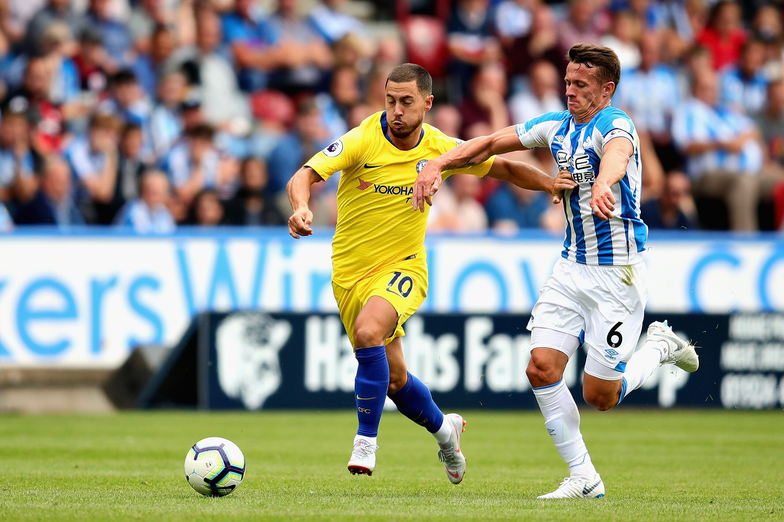 HUDDERSFIELD, ENGLAND - AUGUST 11: Eden Hazard of Chelsea is challenged by Jonathan Hogg of Huddersfield Town during the Premier League match between Huddersfield Town and Chelsea FC at John Smith's Stadium on August 11, 2018 in Huddersfield, United Kingd