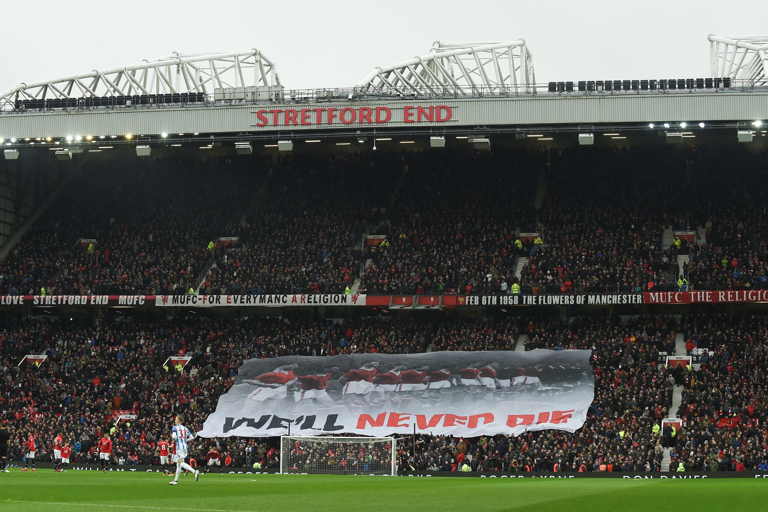 A banner that reads 'we'll never die' travels across the Stretford End in comemmoration of the 1958 Munich Air Disaster in the 60th anniversary year of the crash that killed 23 during the English Premier League football match between Manchester United and