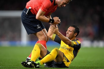 LONDON, ENGLAND - SEPTEMBER 28:  Santi Cazorla of Arsenal is helped to his feet by referee Danny Makkelie during the UEFA Champions League group A match between Arsenal FC and FC Basel 1893 at the Emirates Stadium on September 28, 2016 in London, England.