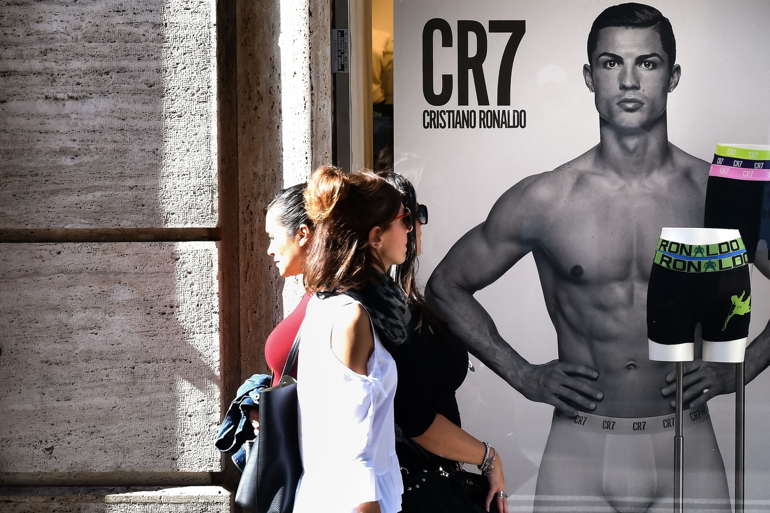 Passersby walk past an advertising poster for an underwear brand, showing a picture of Juventus' Portuguese forward Cristiano Ronaldo in a shop window, on October 9, 2018 in downtown Rome. - Cristiano Ronaldo faces rape allegations after US police on Octo