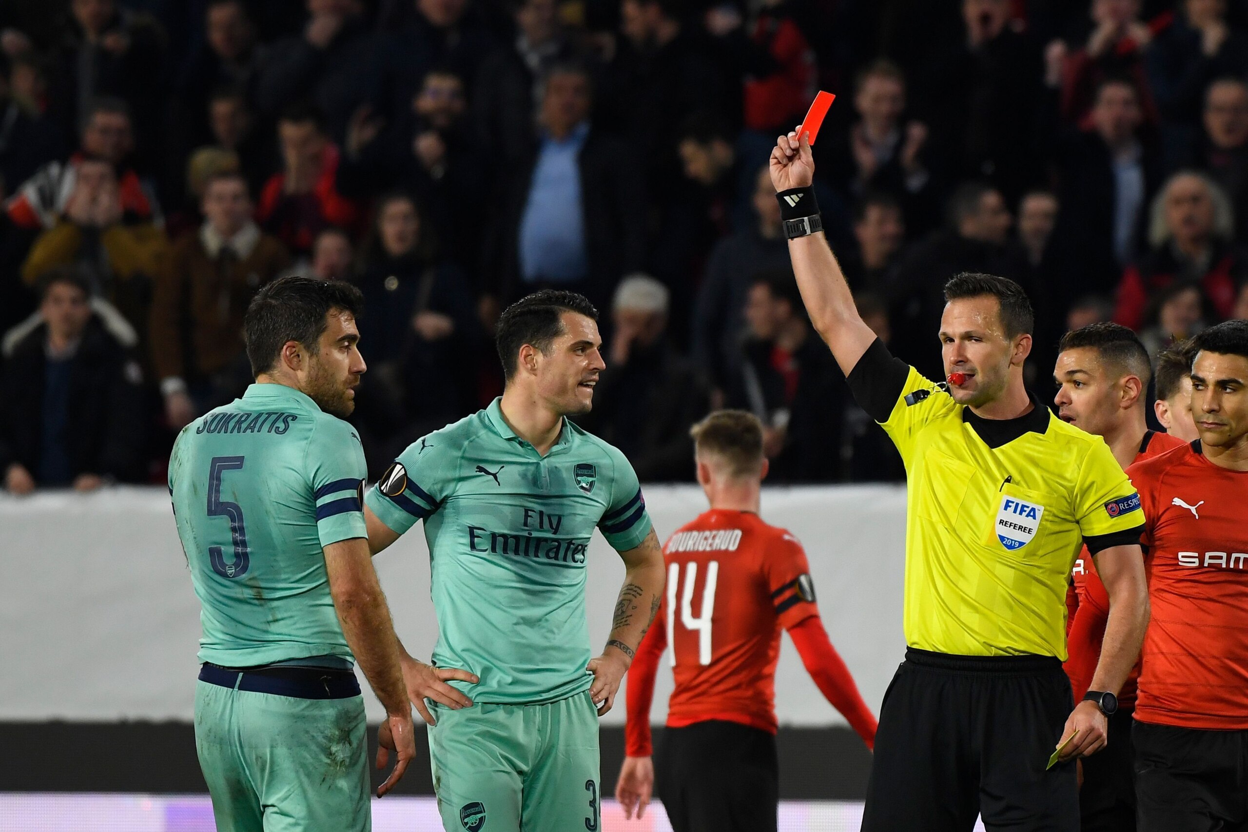 Slovak referee Ivan Kruzliak (R) shows a red card to Arsenal's Greek defender Sokratis Papastathopoulos (L) during the UEFA Europa League round of 16 first leg football match between Stade Rennais FC and Arsenal FC at the Roazhon Park stadium in Rennes, n