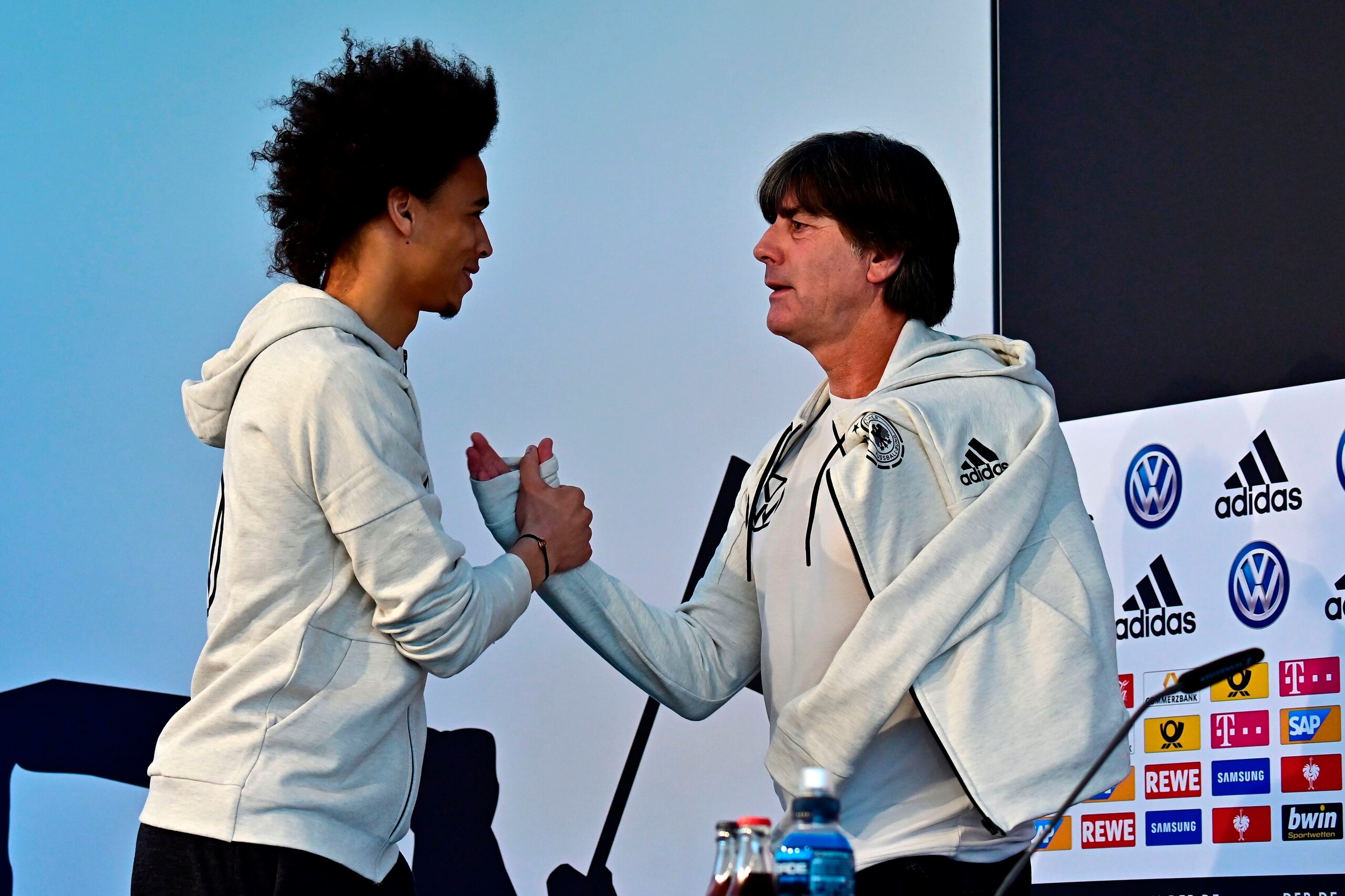 German national football team's player Leroy Sane (L) shakes hands with Germany's head coach Joachim Loew as he arrives on stage to attend a press conference on the eve of the friendly football match Germany v Serbia in Wolfsburg on March 19, 2019. (Photo