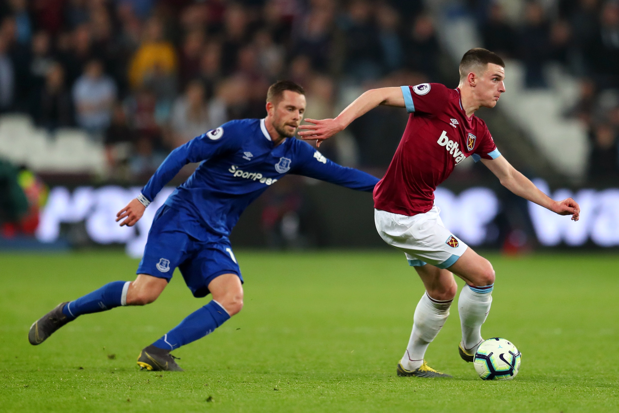 LONDON, ENGLAND - MARCH 30:  Declan Rice of West Ham United runs with the ball under pressure from Gylfi Sigurdsson of Everton during the Premier League match between West Ham United and Everton FC at London Stadium on March 30, 2019 in London, United Kin