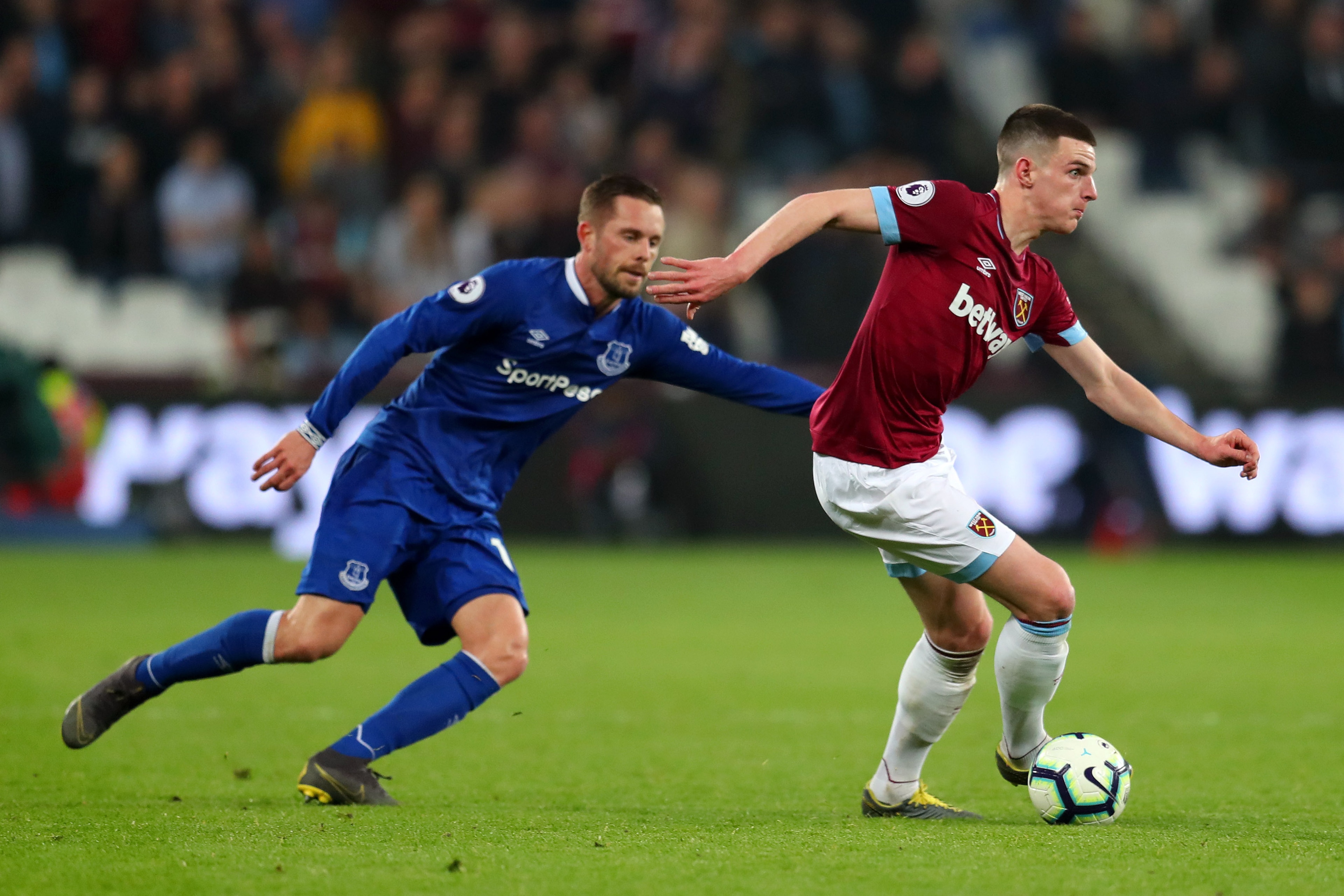 LONDON, ENGLAND - MARCH 30:  Declan Rice of West Ham United runs with the ball under pressure from Gylfi Sigurdsson of Everton during the Premier League match between West Ham United and Everton FC at London Stadium on March 30, 2019 in London, United Kin