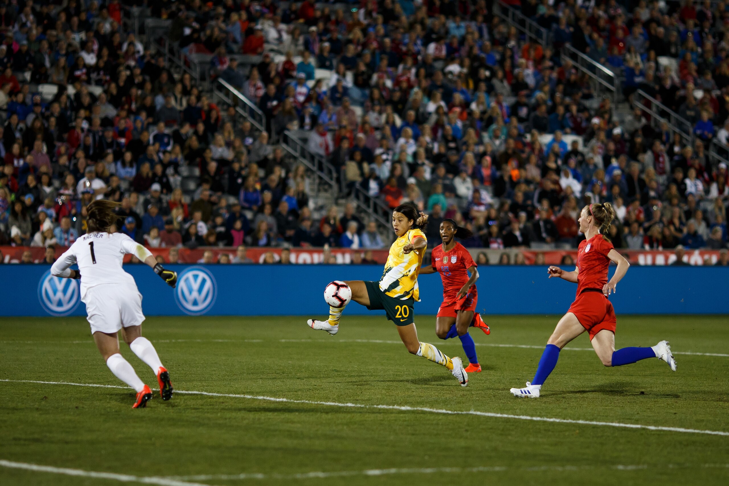 COMMERCE CITY, CO - APRIL 4:  Sam Kerr #20 of Australia splits the defense and takes a shot as Alyssa Naeher #1, Crystal Dunn #19 and Becky Sauerbrunn #4 of the United States defend during the first half at Dick's Sporting Goods Park on April 4, 2019 in C