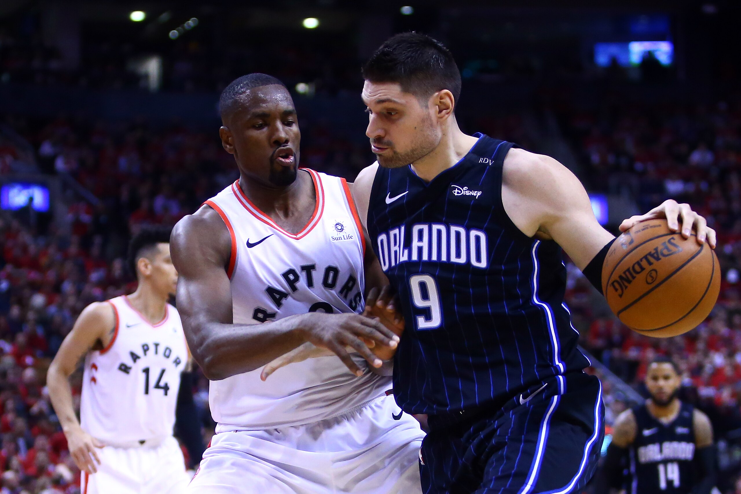 TORONTO, ON - APRIL 13:  Nikola Vucevic #9 of the Orlando Magic dribbles the ball as Serge Ibaka #9 of the Toronto Raptors defends during Game One of the first round of the 2019 NBA playoffs at Scotiabank Arena on April 13, 2019 in Toronto, Canada.  NOTE 