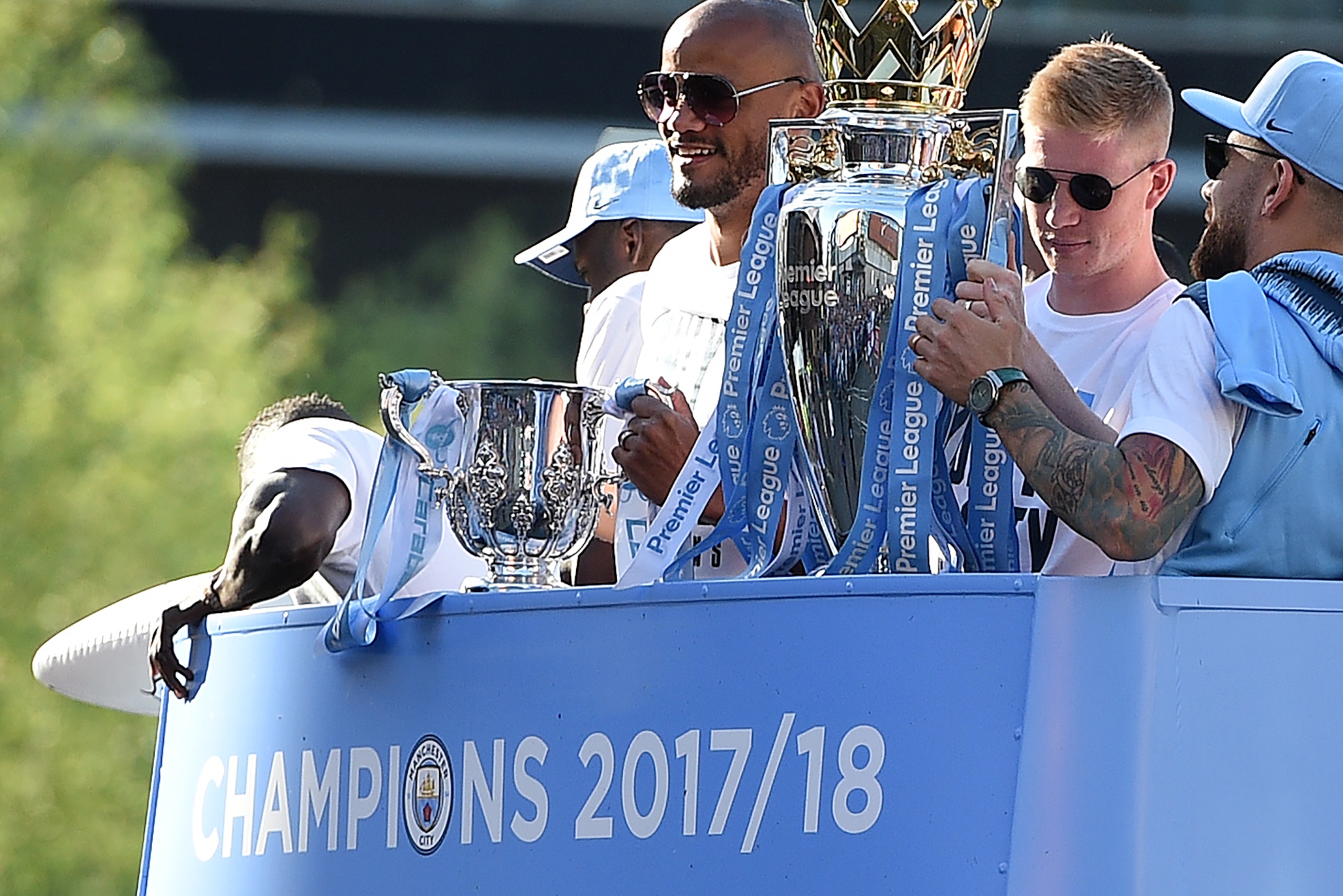 Manchester City's Belgian midfielder Kevin De Bruyne (2R) holds up the Preimer Leagu trophy as Manchester City's Belgian defender Vincent Kompany (C) holds up the English League Cup trophy to fans as the Manchester City team take part in an open-top bus p
