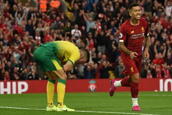Norwich City's Scottish defender Grant Hanley (L) reacts after scoring an own goal as Liverpool's Brazilian midfielder Roberto Firmino celebrates the first goal during the English Premier League football match between Liverpool and Norwich City at Anfield