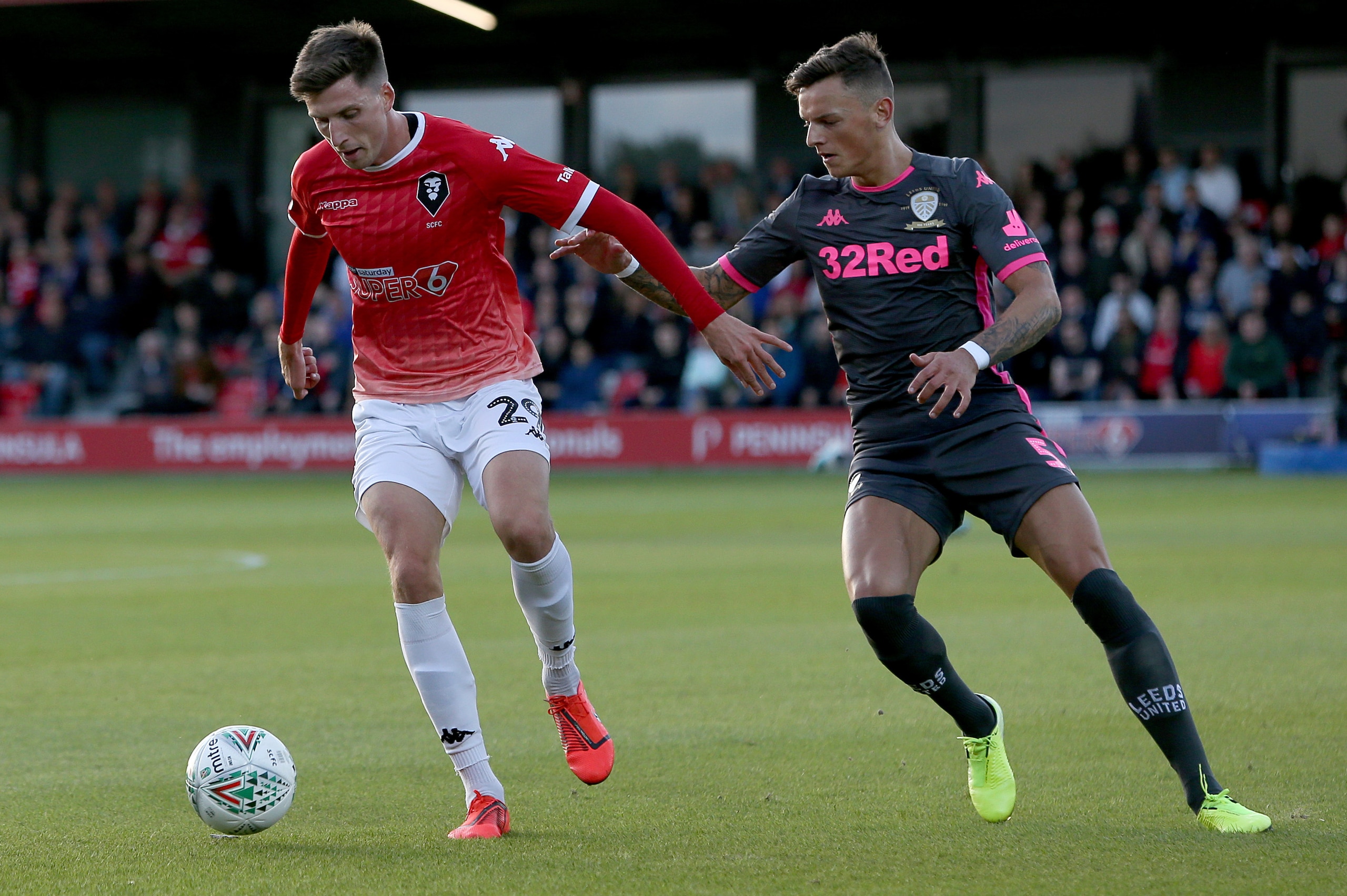 SALFORD, ENGLAND - AUGUST 13: Ben White of Leeds United and Jake Beesley of Salford City compete for the ball during the Carabao Cup First Round match between Salford City and Leeds United at Moor Lane on August 13, 2019 in Salford, England. (Photo by Cha