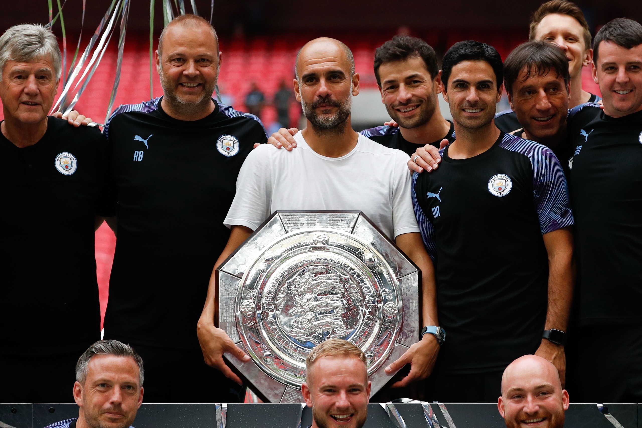Manchester City's Spanish manager Pep Guardiola (C) holds the trophy as he poses with his staff after winning the English FA Community Shield football match between Manchester City and Liverpool at Wembley Stadium in north London on August 4, 2019. (Photo