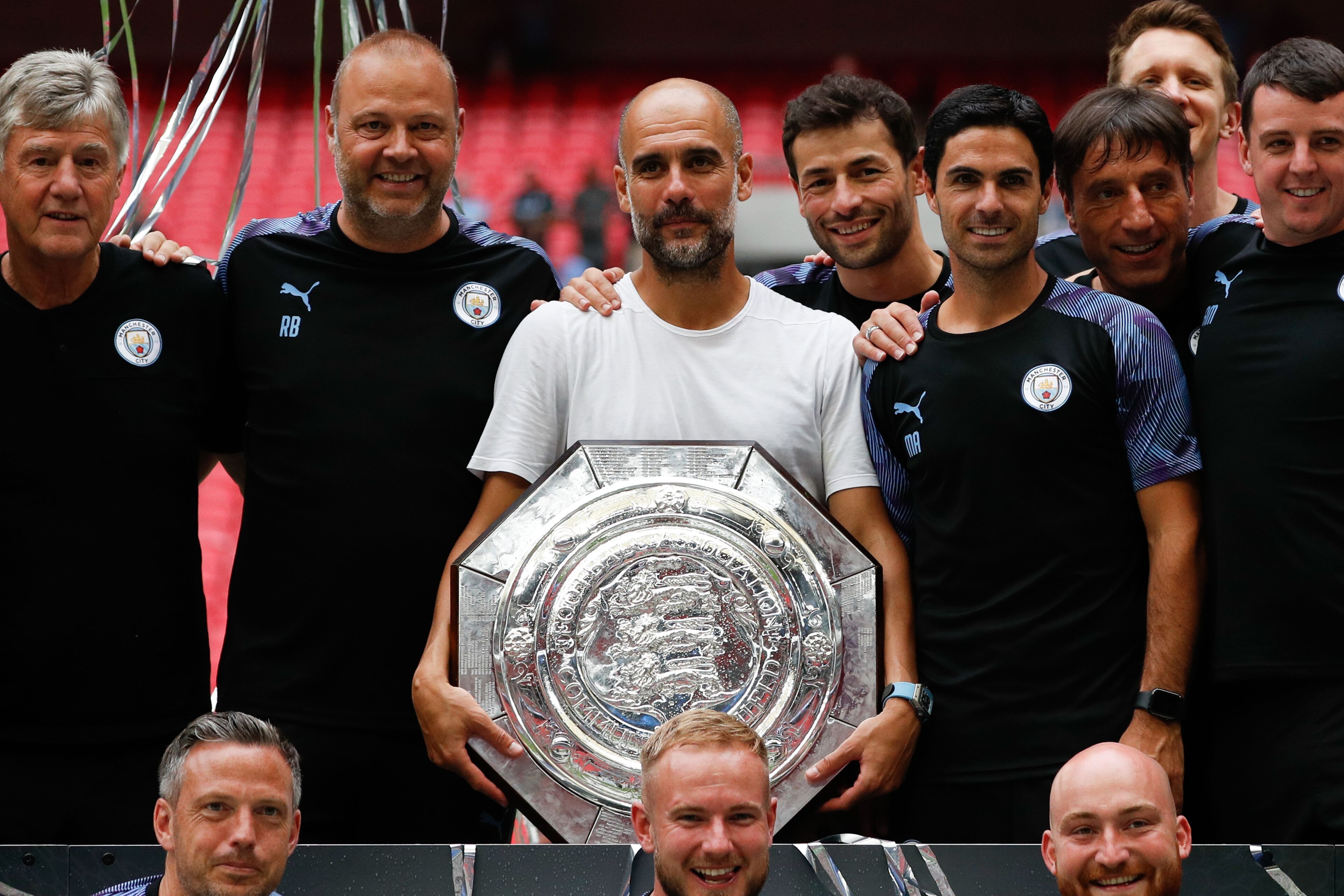 Manchester City's Spanish manager Pep Guardiola (C) holds the trophy as he poses with his staff after winning the English FA Community Shield football match between Manchester City and Liverpool at Wembley Stadium in north London on August 4, 2019. (Photo
