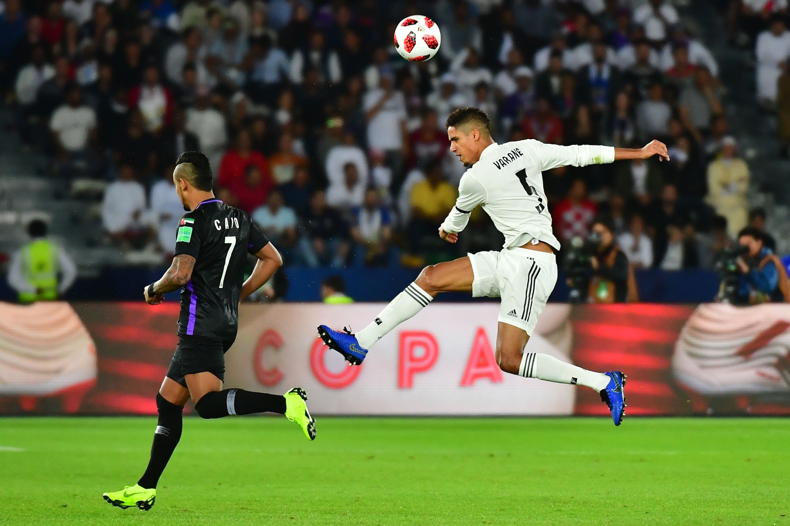 Real Madrid's French defender Raphael Varane (R) clears the ball ahead of Al-Ain's midfielder Caio during the Final match in the FIFA Club World Cup football competition between Real Madrid and Al-Ain at the Zayed Sports City Stadium in Abu Dhabi, the cap