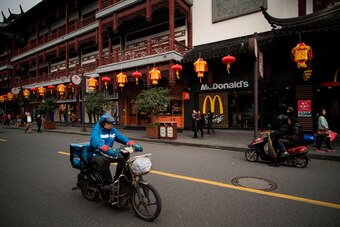 A man drives his scooter past a McDonald's fast food restaurant in Shanghai on January 9, 2017. 
US fast-food giant McDonalds will sell a controlling stake in its China and Hong Kong business for up to 2.08 billion USD to a consortium including state-owne