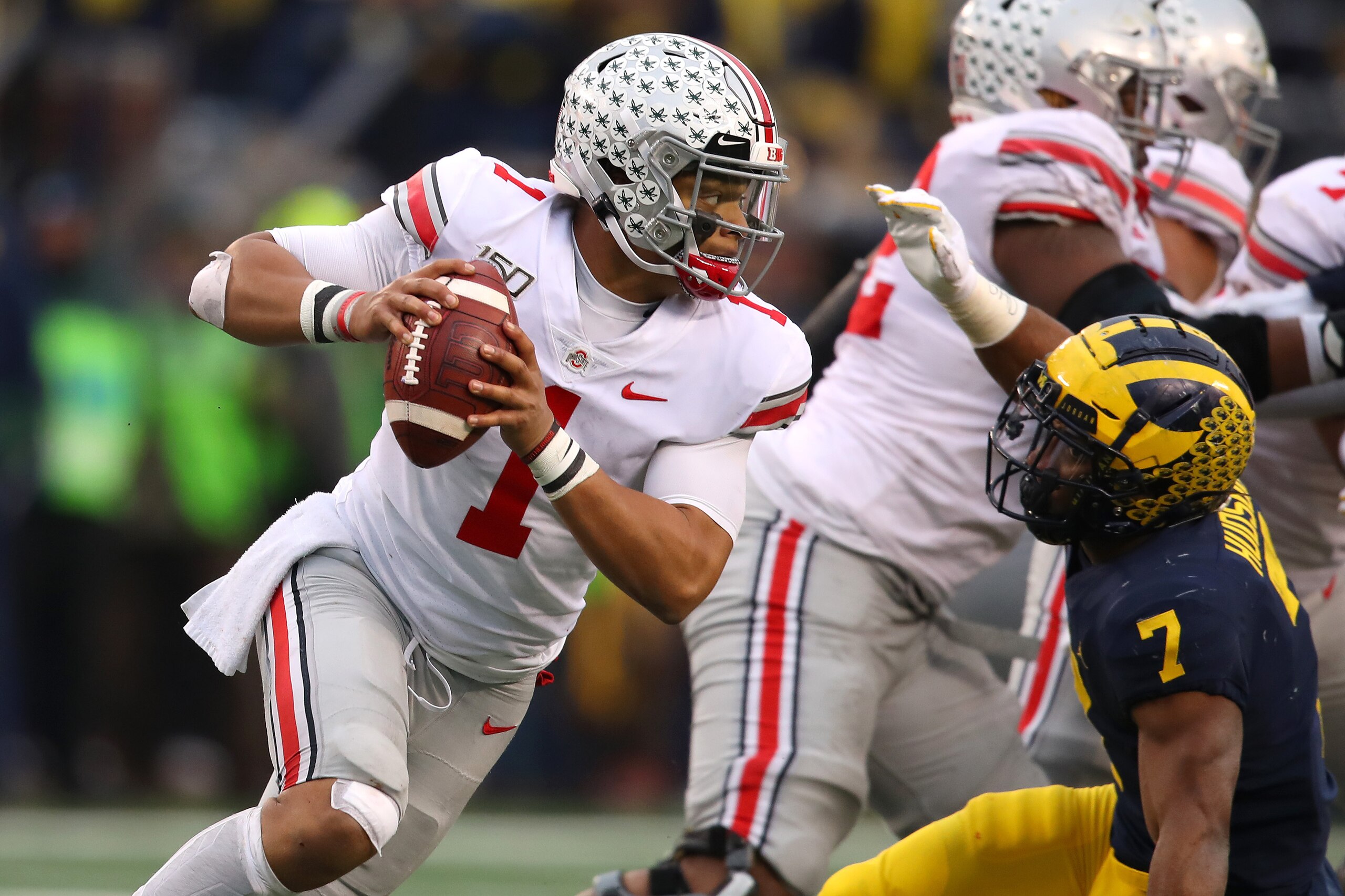 ANN ARBOR, MICHIGAN - NOVEMBER 30: Justin Fields #1 of the Ohio State Buckeyes tries to get around the tackle of Khaleke Hudson #7 of the Michigan Wolverines during the second half at Michigan Stadium on November 30, 2019 in Ann Arbor, Michigan. Ohio Stat