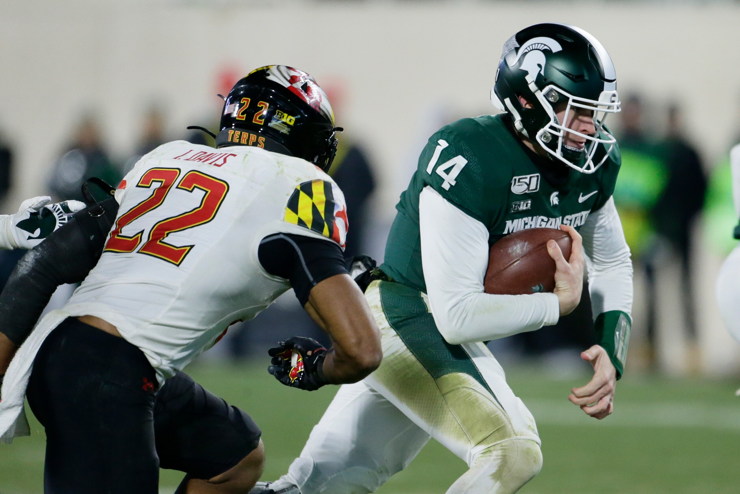 EAST LANSING, MI -  NOVEMBER 30:   Quarterback Brian Lewerke #14 of the Michigan State Spartans is pursued by linebacker Isaiah Davis #22 of the Maryland Terrapins during the second half at Spartan Stadium on November 30, 2019, in East Lansing, Michigan. 