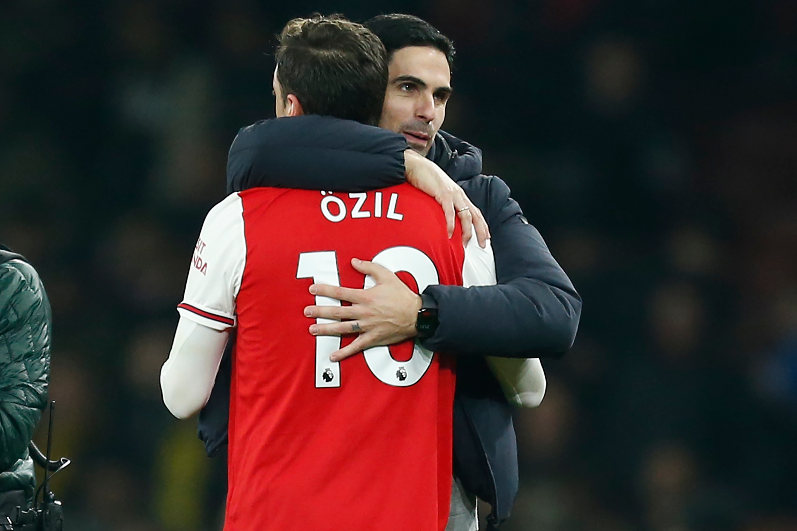 Arsenal's Spanish head coach Mikel Arteta (R) embraces Arsenal's German midfielder Mesut Ozil (L) on the pitch after the English Premier League football match between Arsenal and Manchester United at the Emirates Stadium in London on January 1, 2020. - Ar
