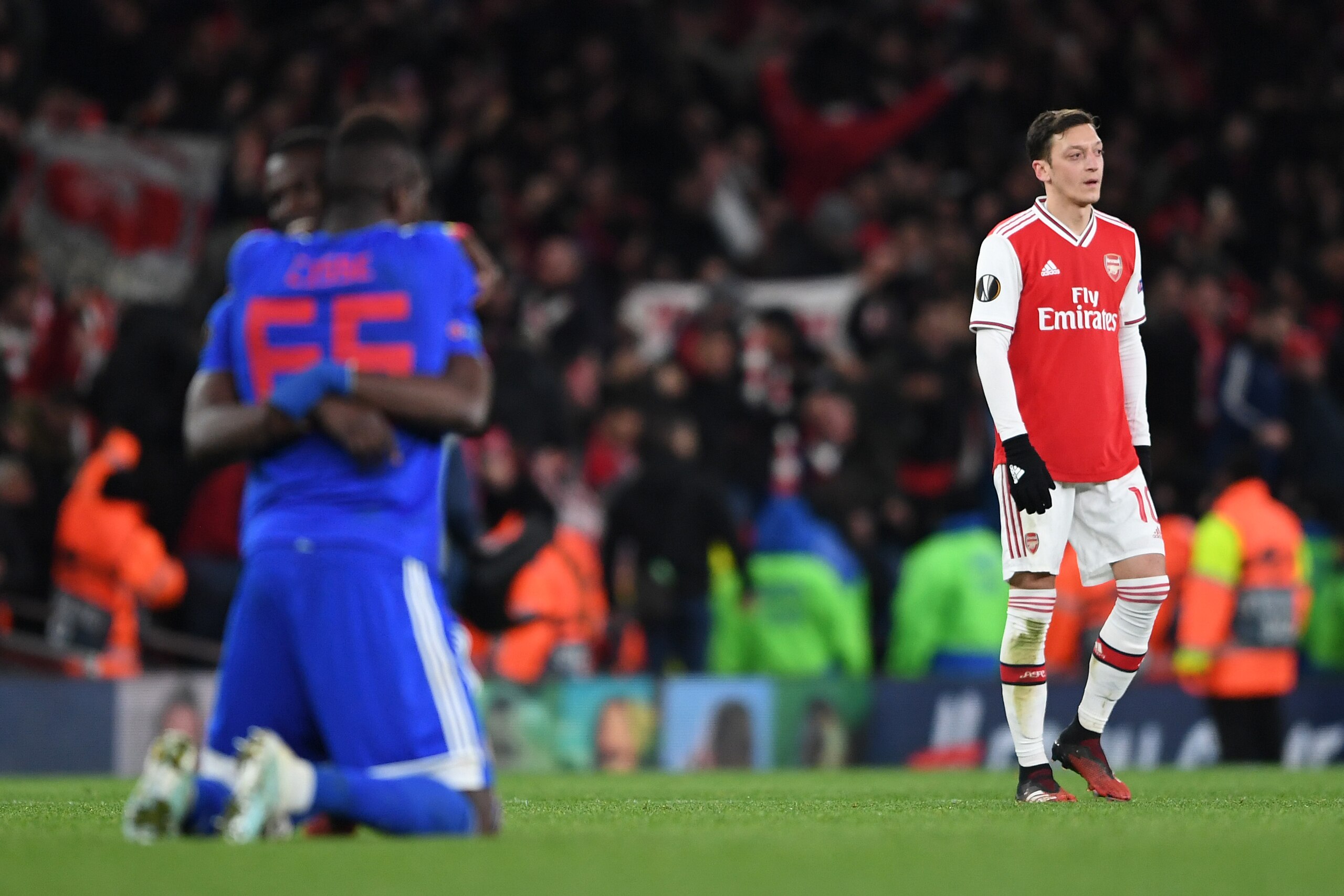 LONDON, ENGLAND - FEBRUARY 27: Mesut Ozil of Arsenal looks dejected as Papa Abou Cisse of Olympiacos celebrates following Olympiacos' victory in the UEFA Europa League round of 32 second leg match between Arsenal FC and Olympiacos FC at Emirates Stadium o