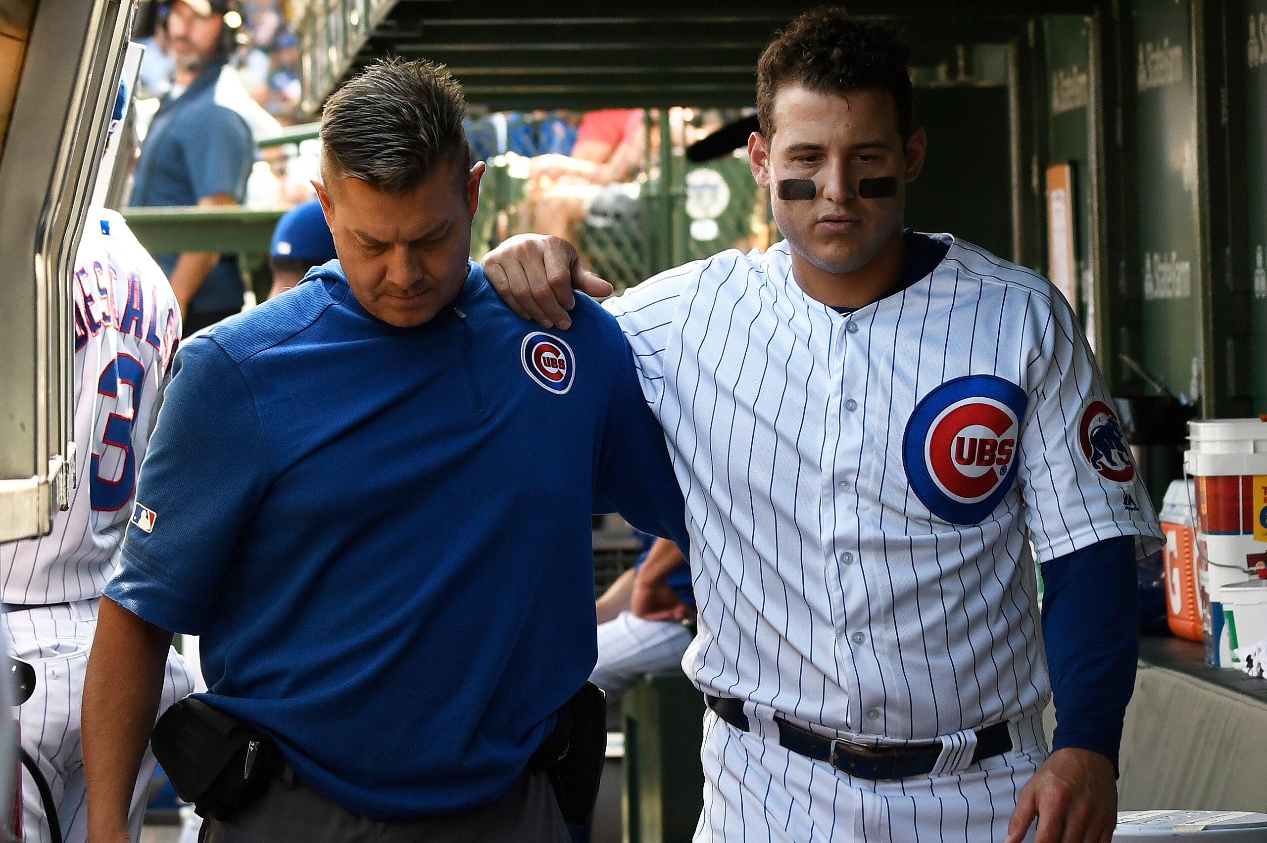 CHICAGO, ILLINOIS - SEPTEMBER 15: Anthony Rizzo #44 of the Chicago Cubs is helped in the dugout by trainer PJ Mainville after being injured against the Pittsburgh Pirates during the third inning at Wrigley Field on September 15, 2019 in Chicago, Illinois.