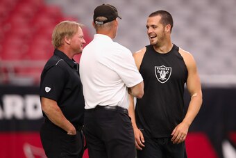 GLENDALE, ARIZONA - AUGUST 15:  (L-R) Head coach Jon Gruden, general manager Mike Mayock and quarterback Derek Carr #4 of the Oakland Raiders talk on the field before the NFL preseason game against the Arizona Cardinals at State Farm Stadium on August 15,