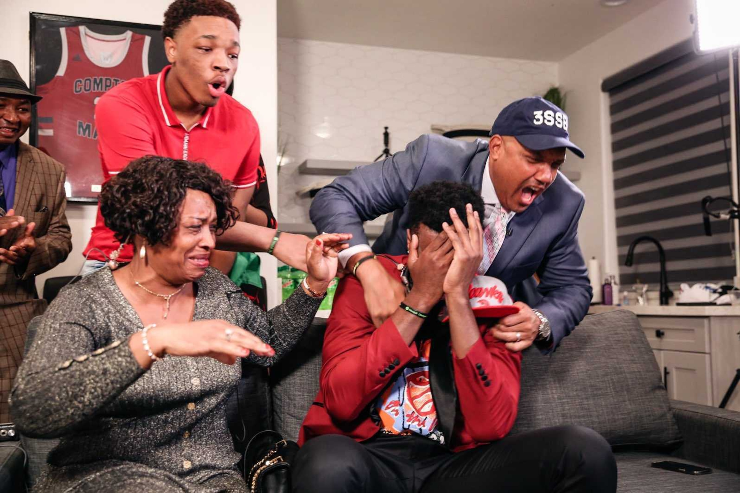 Onyeka Okongwu, bottom right, reacts to news of going No. 6 overall in the 2020 draft, with his Compton Magic jersey hanging on the wall behind him and coach Etop Udo-Ema over his shoulder.