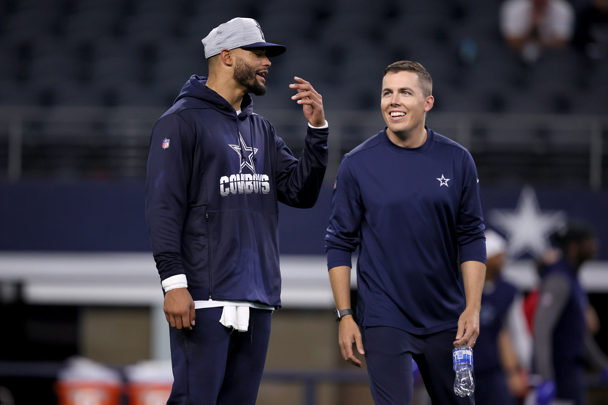 ARLINGTON, TEXAS - AUGUST 21: Quarterback Dak Prescott #4 of the Dallas Cowboys talks with offensive coordinator Kellen Moore of the Dallas Cowboys on the field during pregame warm-ups before the Dallas Cowboys take on the Houston Texans in a preseason NF