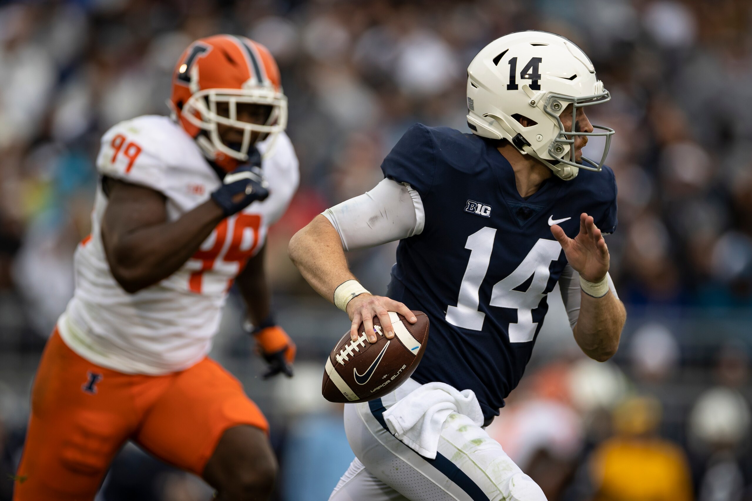 STATE COLLEGE, PA - OCTOBER 23: Sean Clifford #14 of the Penn State Nittany Lions is chased out of the pocket by Owen Carney Jr. #99 of the Illinois Fighting Illini during the second half at Beaver Stadium on October 23, 2021 in State College, Pennsylvani
