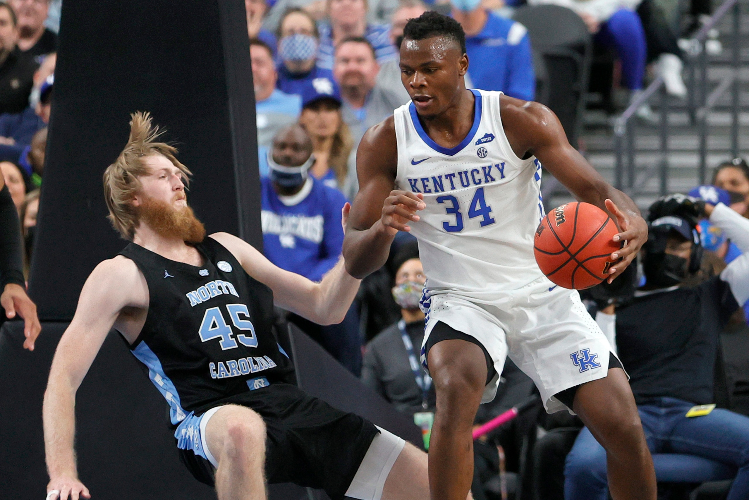 LAS VEGAS, NEVADA - DECEMBER 18:  Brady Manek #45 of the North Carolina Tar Heels falls to the court as Oscar Tshiebwe #34 of the Kentucky Wildcats is called for an offensive foul during the CBS Sports Classic at T-Mobile Arena on December 18, 2021 in Las