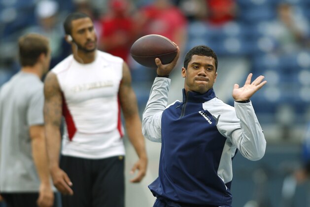 Seattle Seahawks quarterback Russell Wilson, right, passes during team warmups as San Francisco 49ers quarterback Colin Kaepernick, looks on in the background at left, before an NFL football game, Sunday, Sept. 15, 2013, in Seattle. (AP Photo/John Froschauer)