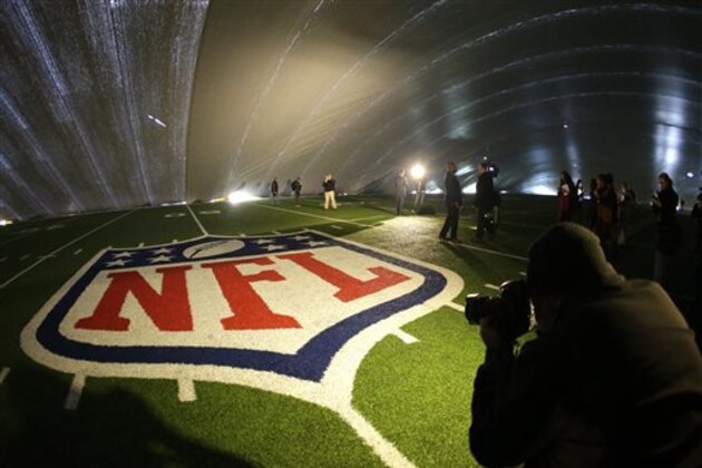 FILE - In this Jan. 15, 2014 file photo, the NFL logo at midfield of MetLife Stadium is illuminated by lights on television reporters' videocameras as members of the media are given a tour under a tarp used by crews to keep the turf dry ahead of Super Bowl XLVIII in East Rutherford, N.J. As the Denver Broncos and Seattle Seahawks prep for their Feb. 2, 2014 showdown in the Super Bowl, a legal fight is playing out over the very turf installed months ago at the NFL title game's venue. Taylor Turf Installation Inc. is suing the MetLife Stadium's operators and the company that hired the suburban St. Louis company, seeking more than $292,000 that Taylor Turf claims it still is owed for hustling to install the  stadium's playing surface last summer. (AP Photo/Julio Cortez, File)