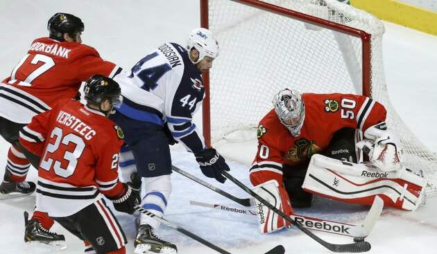 Chicago Blackhawks goalie Corey Crawford (50) makes a save on a shot by Winnipeg Jets defenseman Zach Bogosian (44) as Sheldon Brookbank (17) and Kris Versteeg (23) defend during the first period of an NHL hockey game Sunday, Jan. 26, 2014, in Chicago. (AP Photo/Charlie Arbogast)