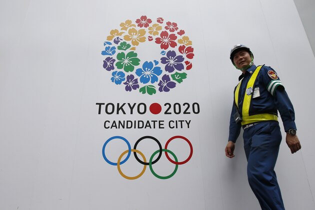 A security guard walks past the logo of Tokyo's bid for the 2020 Olympic Games decorated on a fence of a construction site in Tokyo, Thursday, July 25, 2013. Tokyo is bidding against Istanbul and Madrid. (AP Photo/Shizuo Kambayashi)