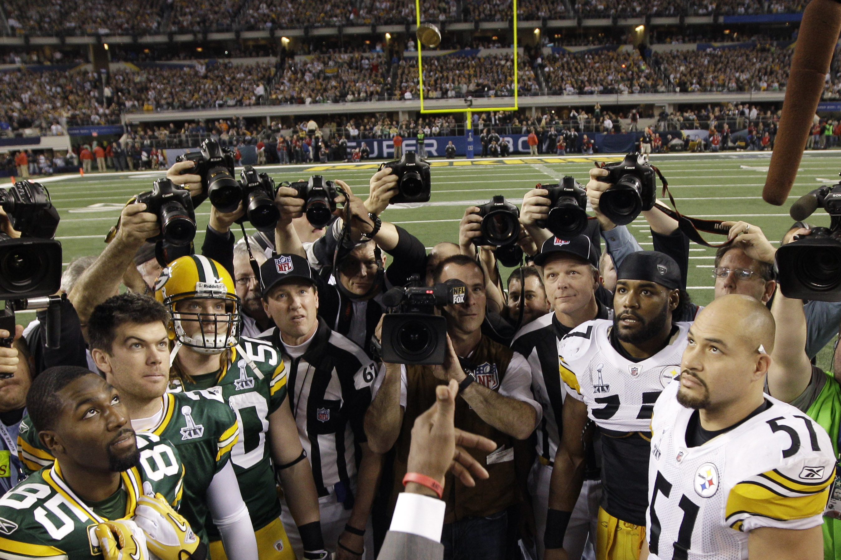 Players look on as former NFL player Deion Sanders tosses the coin during the opening toss before the NFL football Super Bowl XLV game between the Green Bay Packers and the Pittsburgh Steelers Sunday, Feb. 6, 2011, in Arlington, Texas. (AP Photo/David J. Phillip)