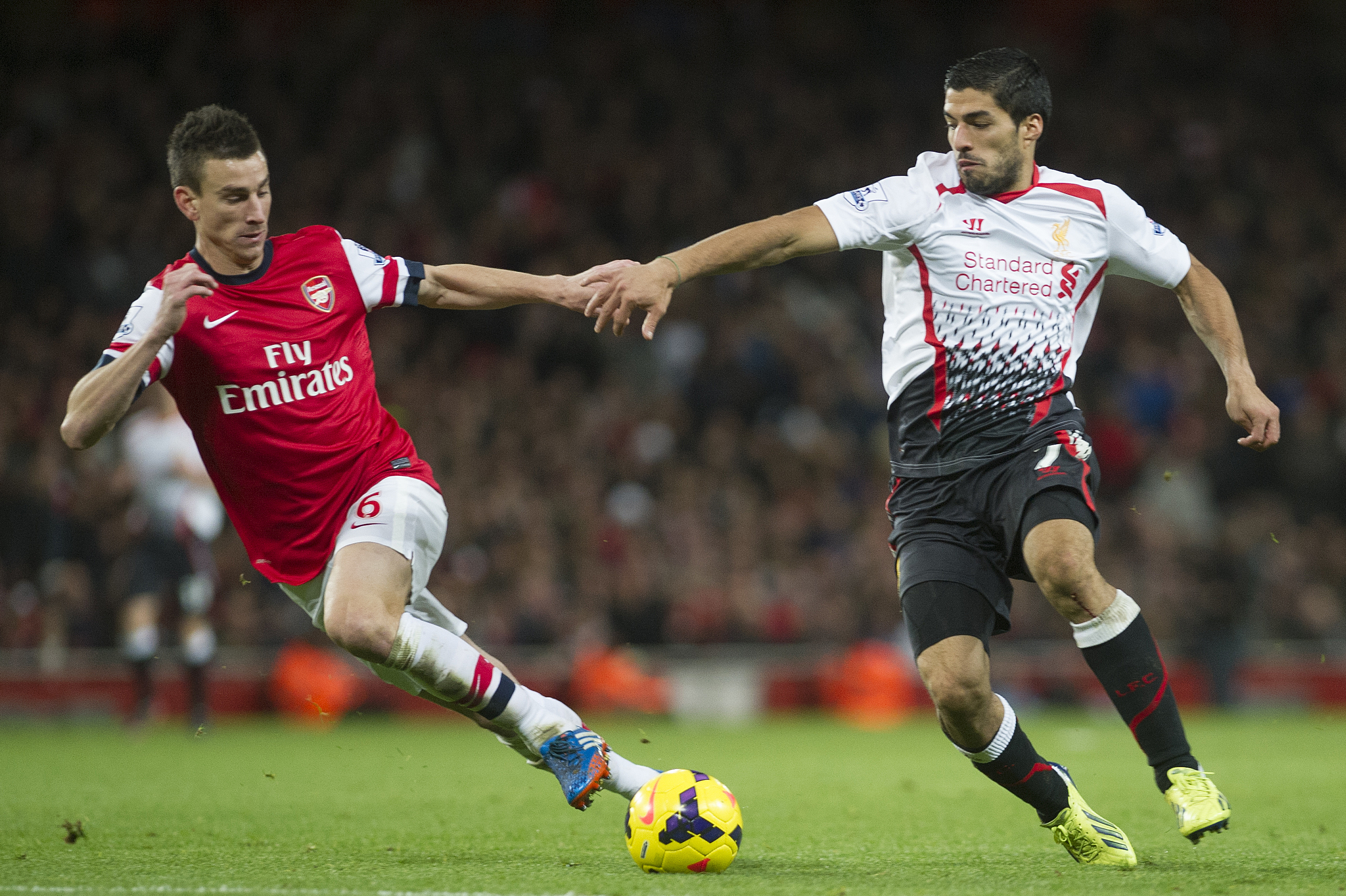 Arsenal's Laurent Koscielny  fights for the ball with Liverpool's Luis Suárez, during their English Premier League soccer match, at the Emirates Stadium, in London, Saturday, Nov. 2, 2013. (AP Photo / Bogdan Maran)