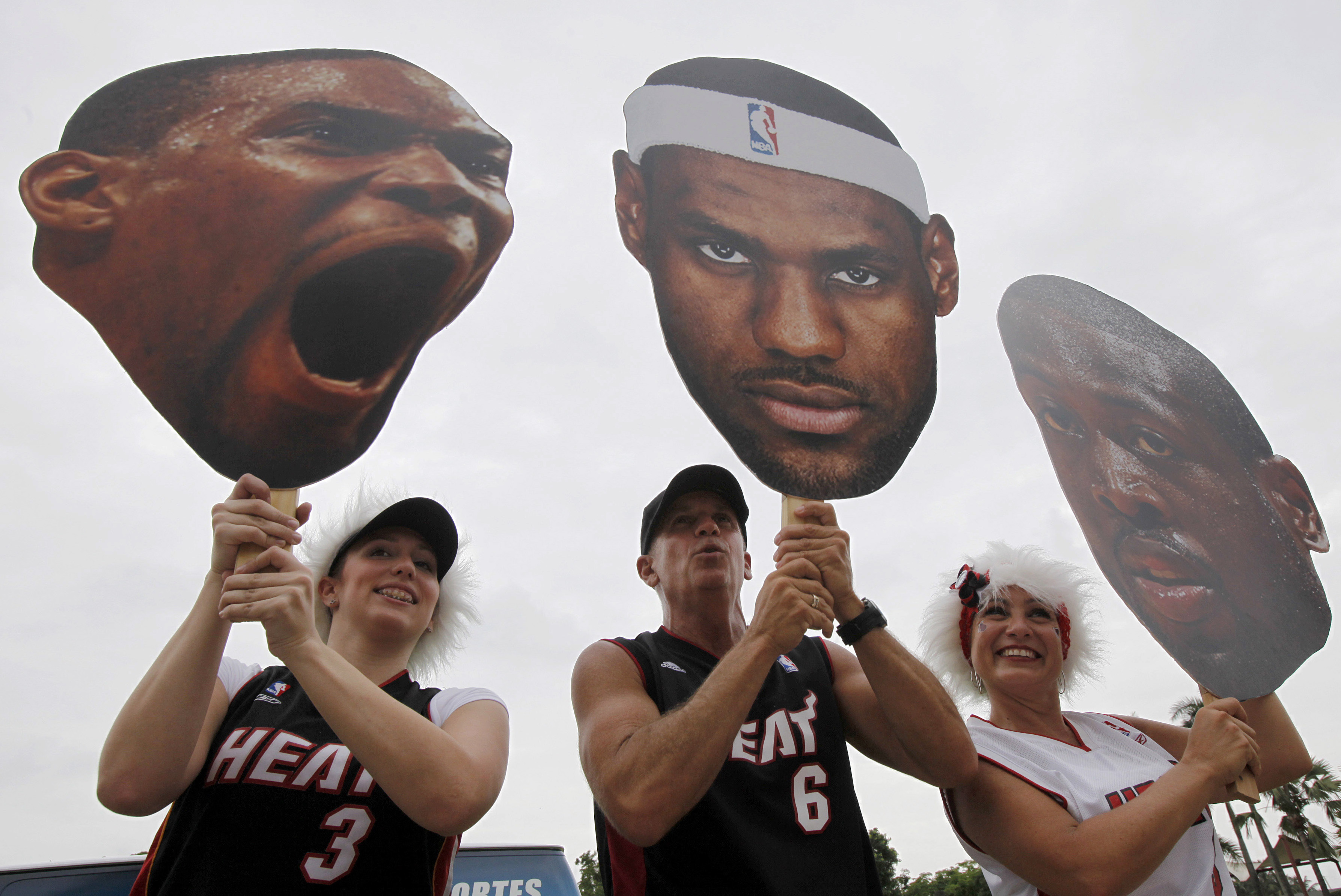 Miami Heat fans Kristal Tamayo, left, Eddie Quintana, center, and his wife Nikki Quintana hold up huge cutout heads of Chris Bosh, LeBron James, and  Dwyane Wade for a parade in Miami, Monday, June 25, 2012 in celebration of winning the NBA Finals basketball championship against the Oklahoma City Thunder. (AP Photo/Wilfredo Lee)