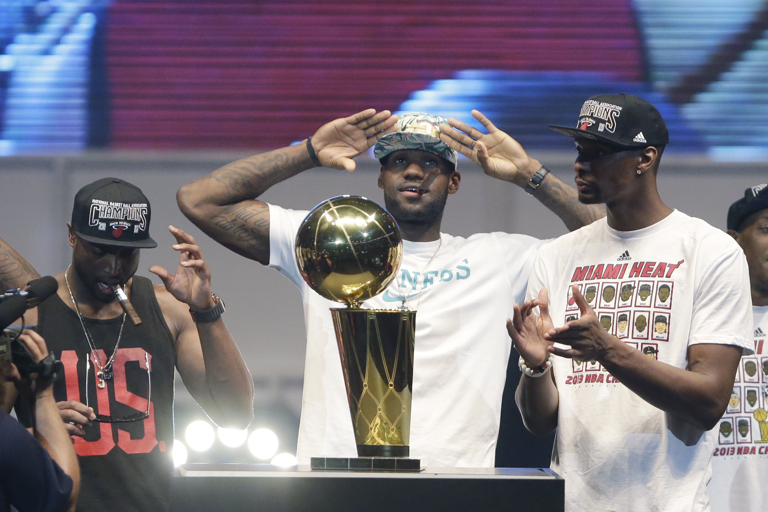 Miami Heat small forward LeBron James, center, salutes the crowd after touching the Larry O'Brien NBA Championship Trophy as shooting guard Dwyane Wade, left, and center Chris Bosh, right, look on, Monday, June 24, 2013 during a celebration for season ticket holders at the American Airlines Arena in Miami. The Heat defeated the San Antonio Spurs 95-88 in Game 7 to win their second straight NBA championship. (AP Photo/Wilfredo Lee)